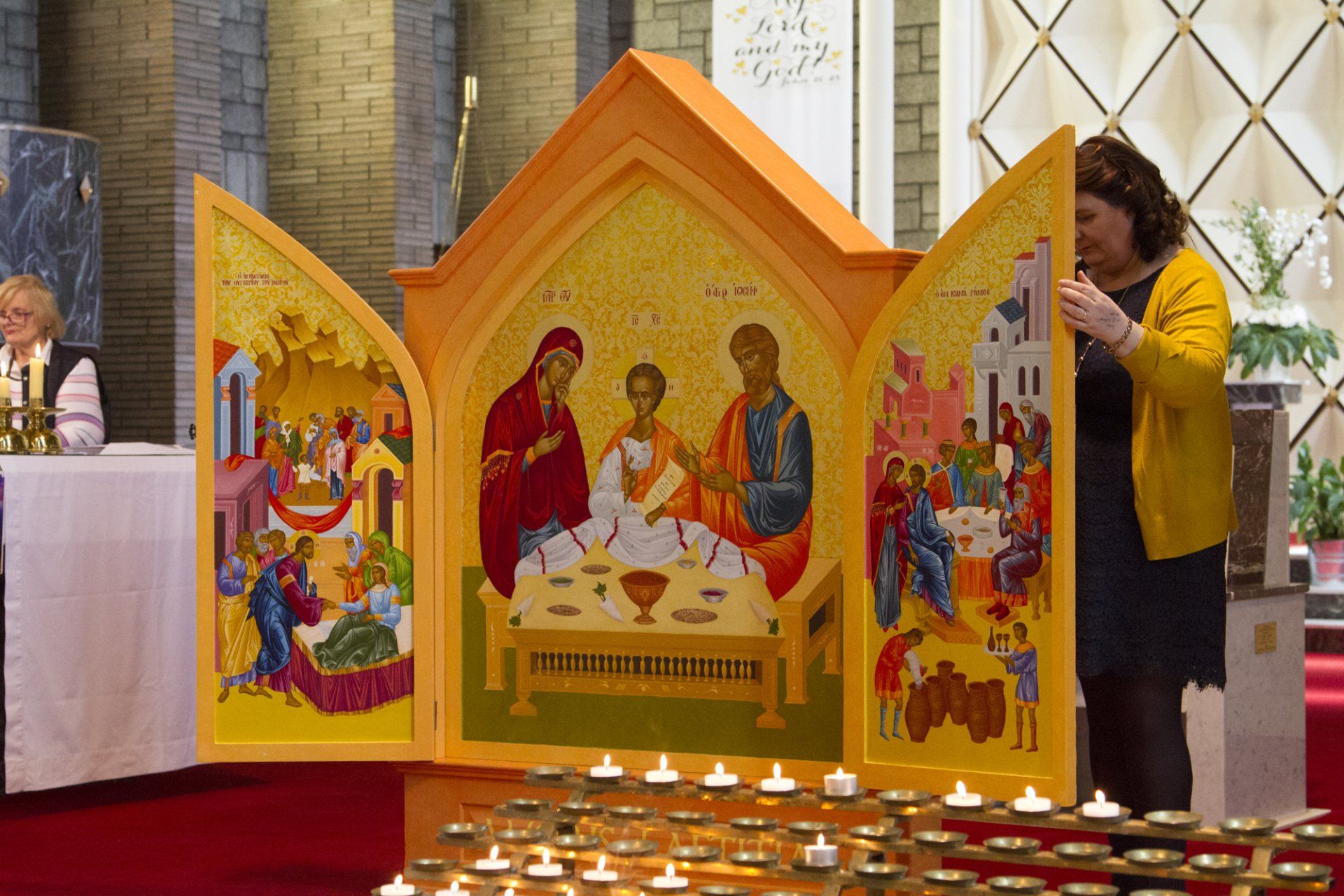A woman in a yellow sweater is standing in front of an icon in a church.