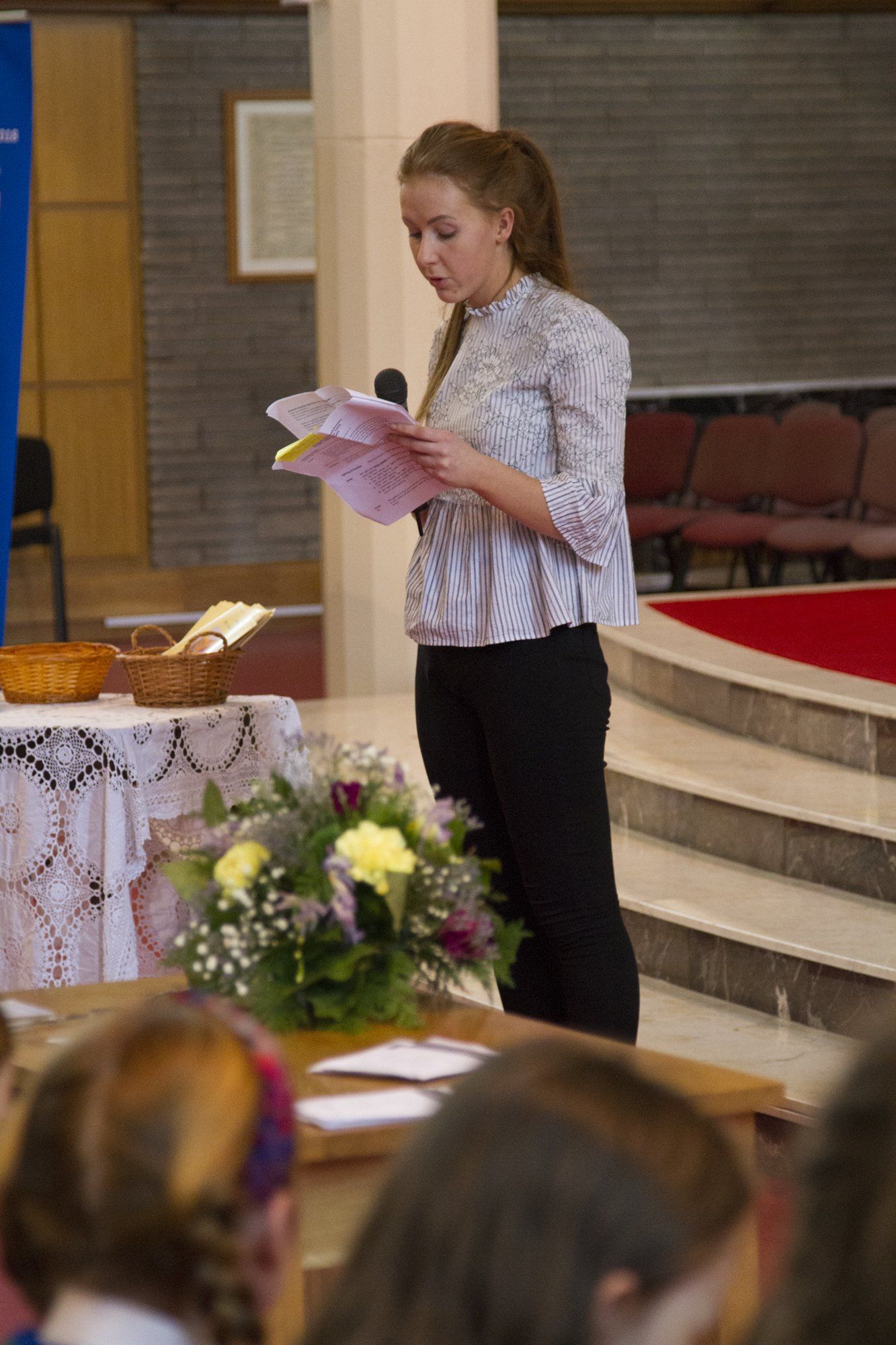 A woman is standing in front of a microphone holding a piece of paper.
