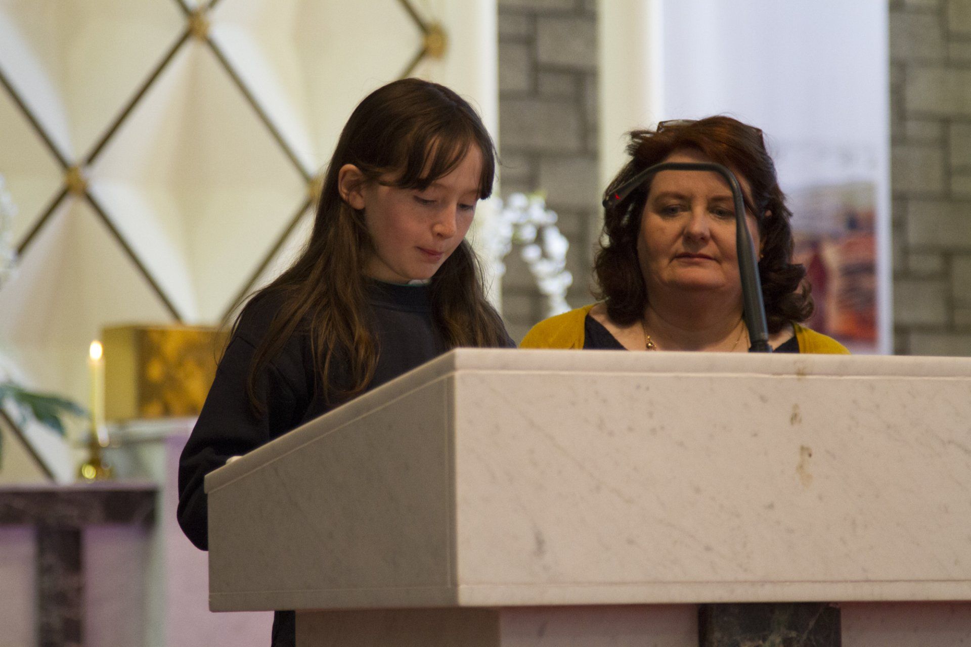 A woman and a girl are standing at a podium in a church.