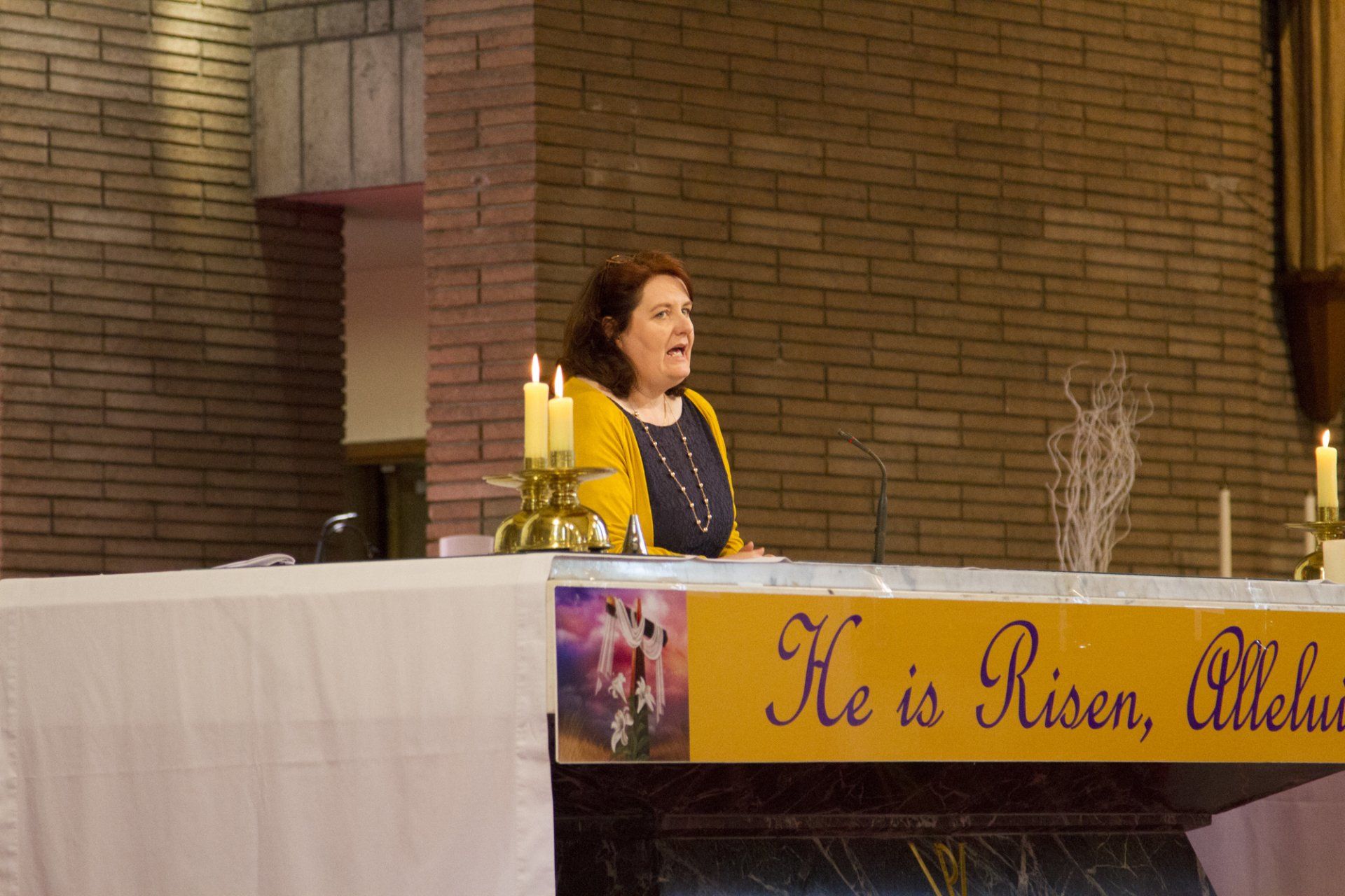 A woman is standing in front of a sign that says he is risen