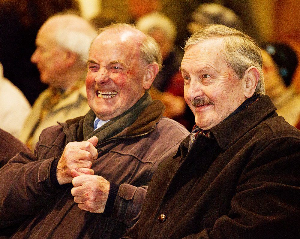 Two older men are sitting next to each other and smiling