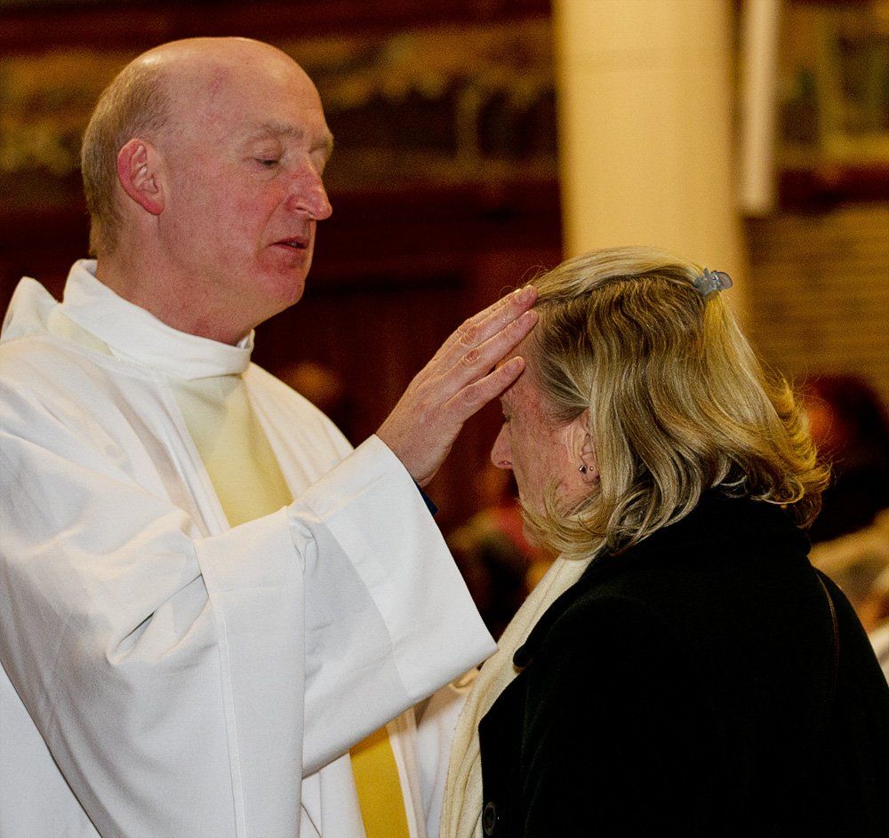 A man in a white robe is blessing a woman 's head