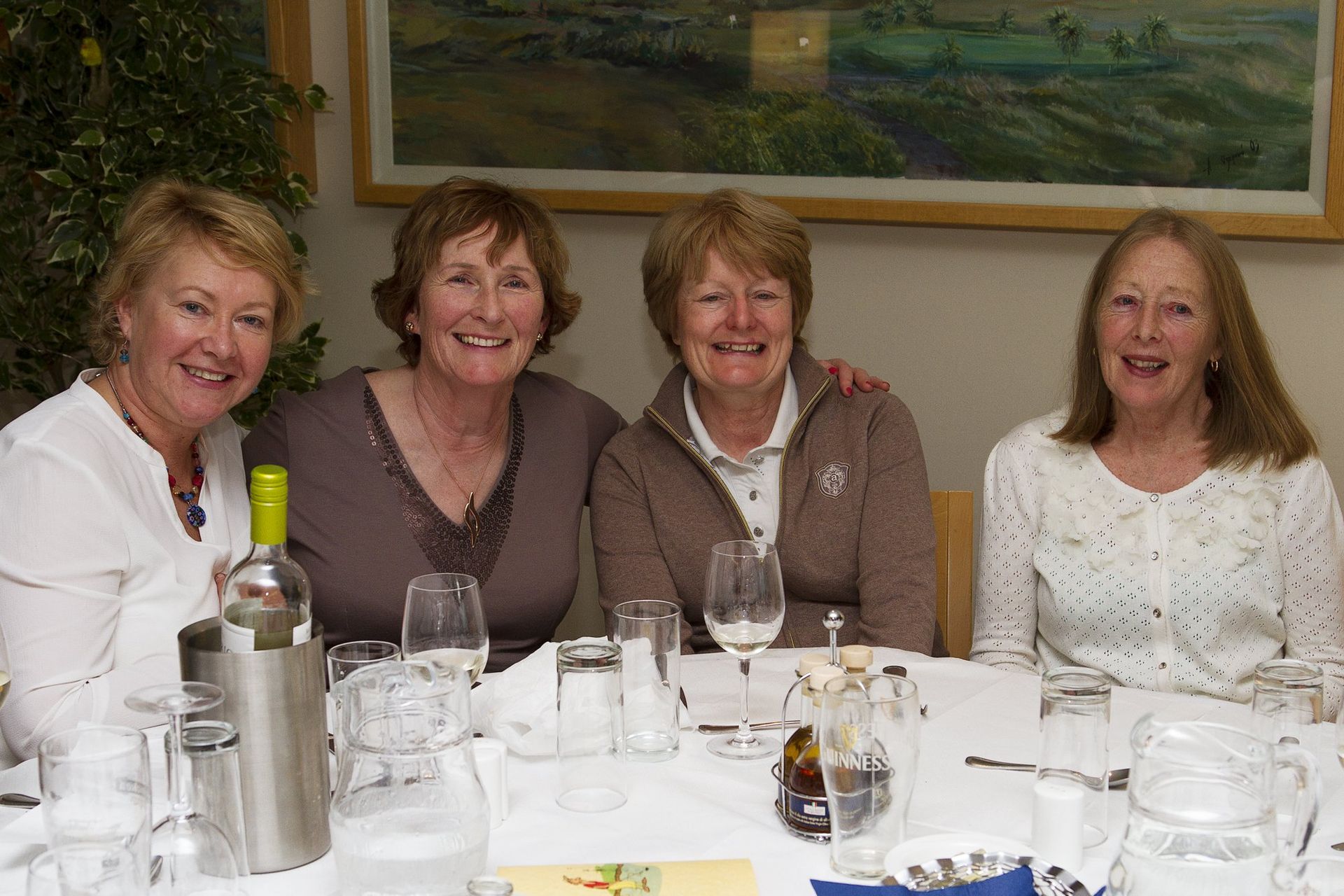 Four women are sitting at a table with wine glasses and smiling.
