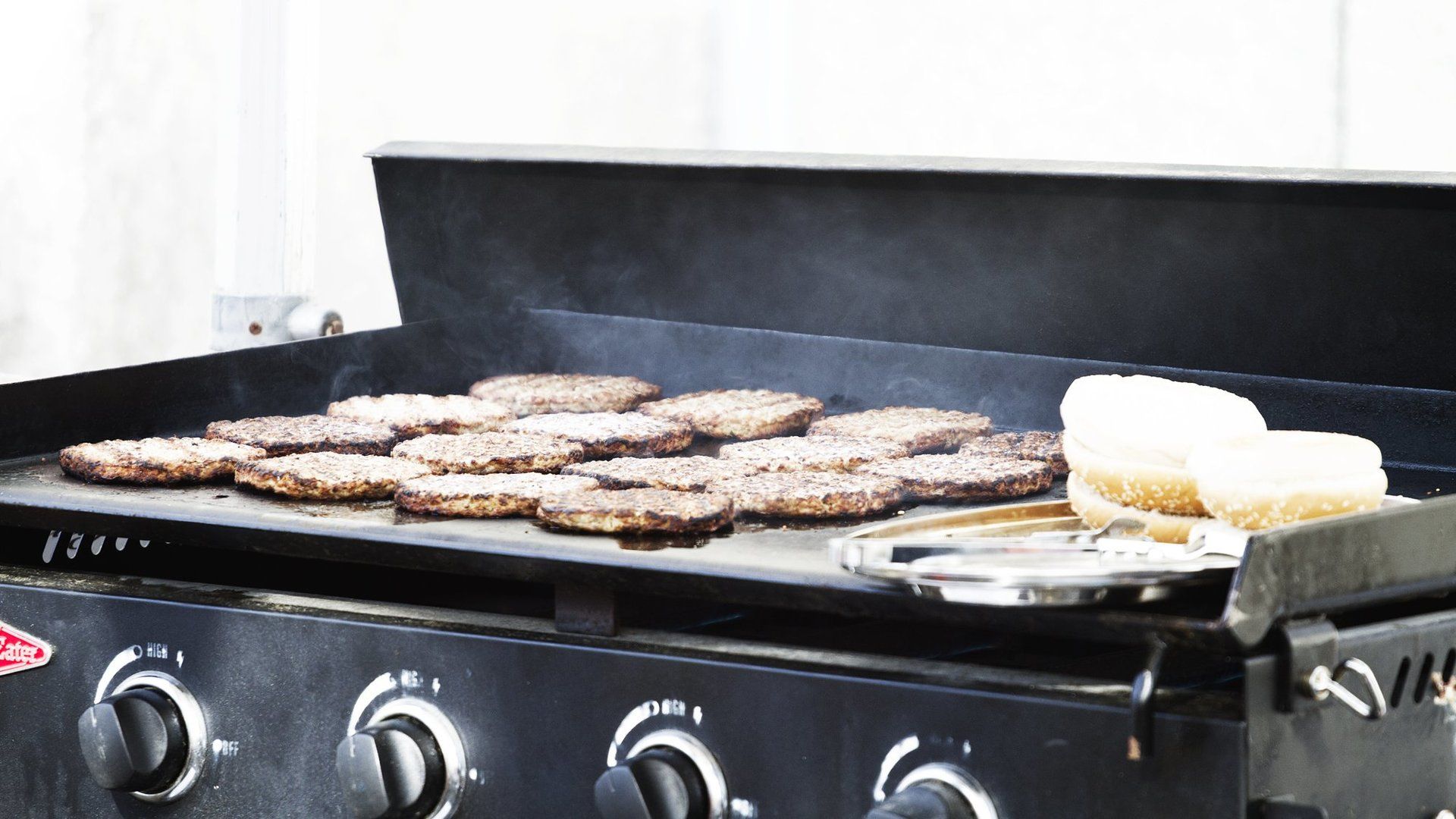 A bunch of hamburgers are cooking on a grill