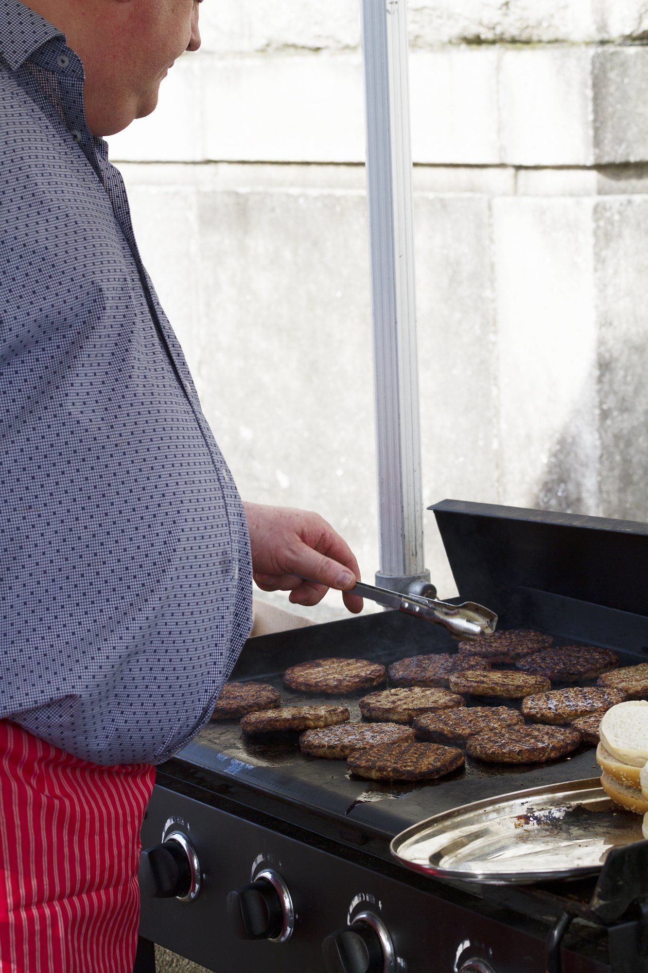 A man is cooking hamburgers on a grill with a spatula.