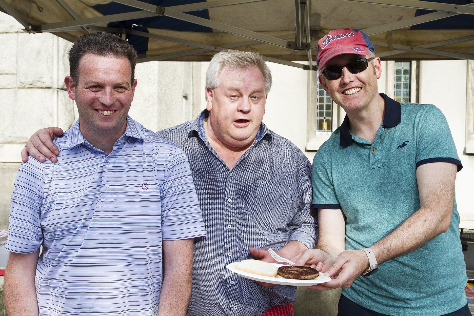 Three men are posing for a picture and one of them is holding a plate of food.