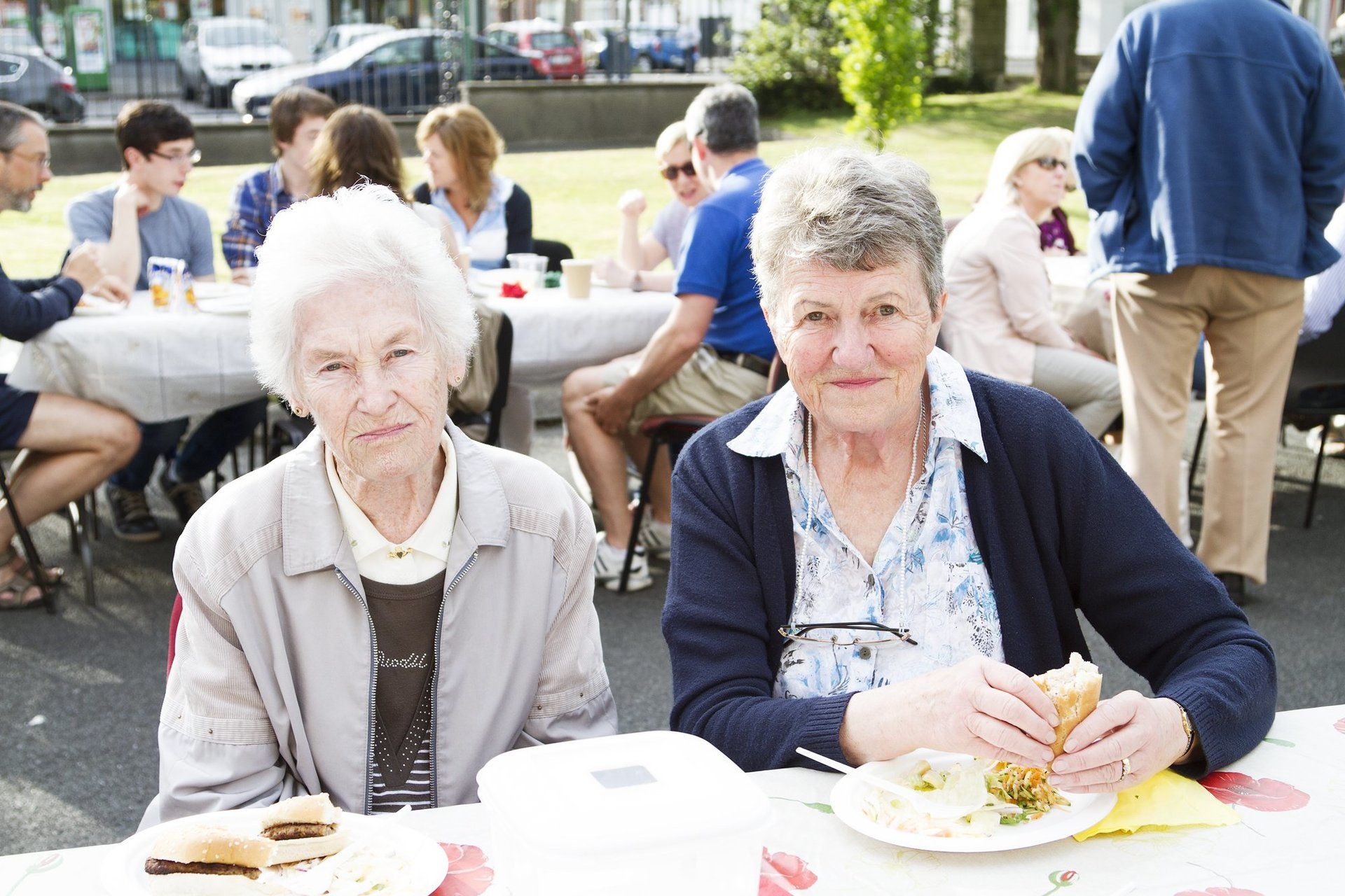 Two older women are sitting at a table eating sandwiches