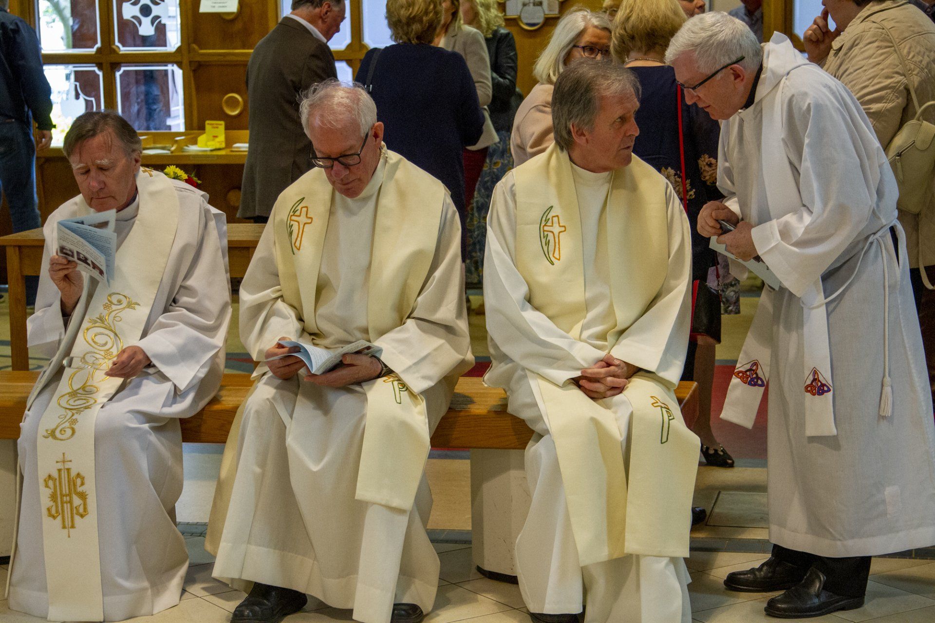 A group of priests are sitting on a bench in a church.