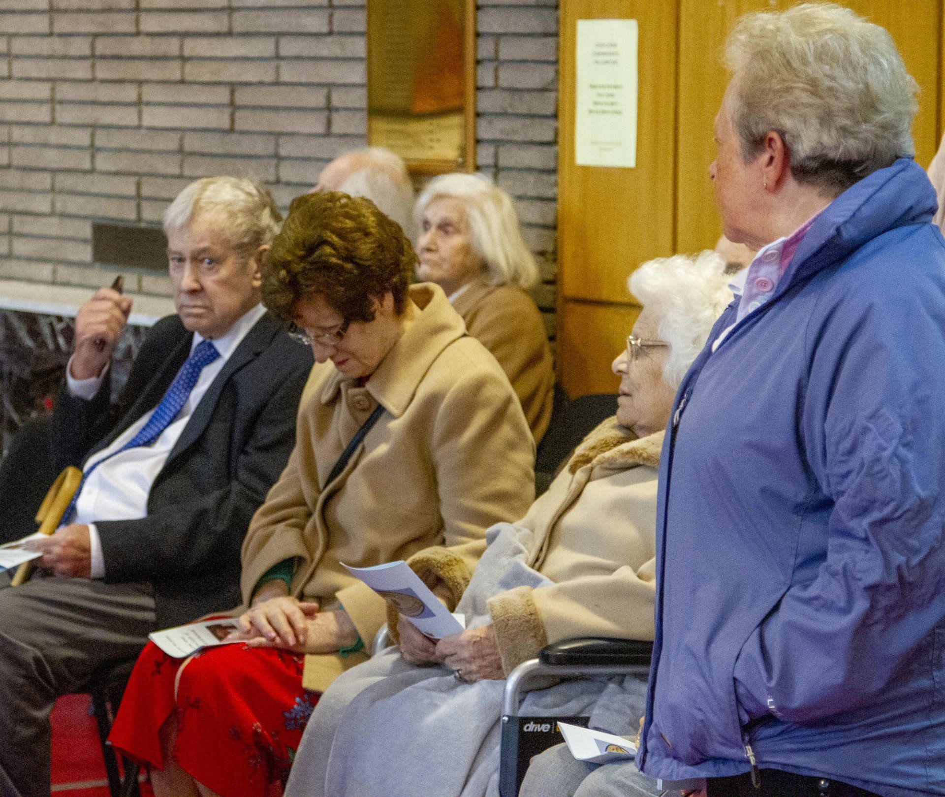 A woman in a blue jacket stands in front of a group of people sitting in chairs