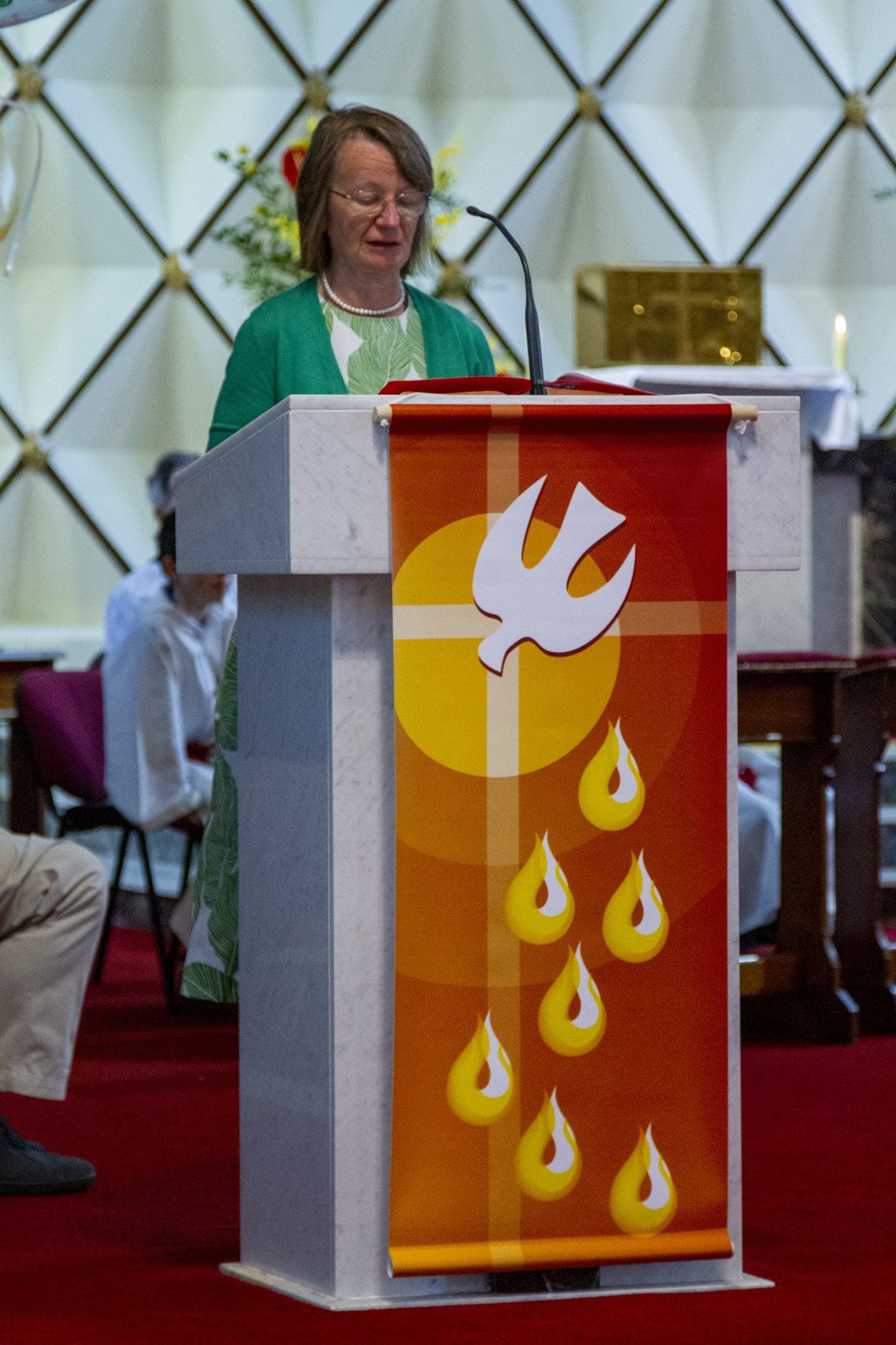 A woman stands at a podium with a banner with a dove on it
