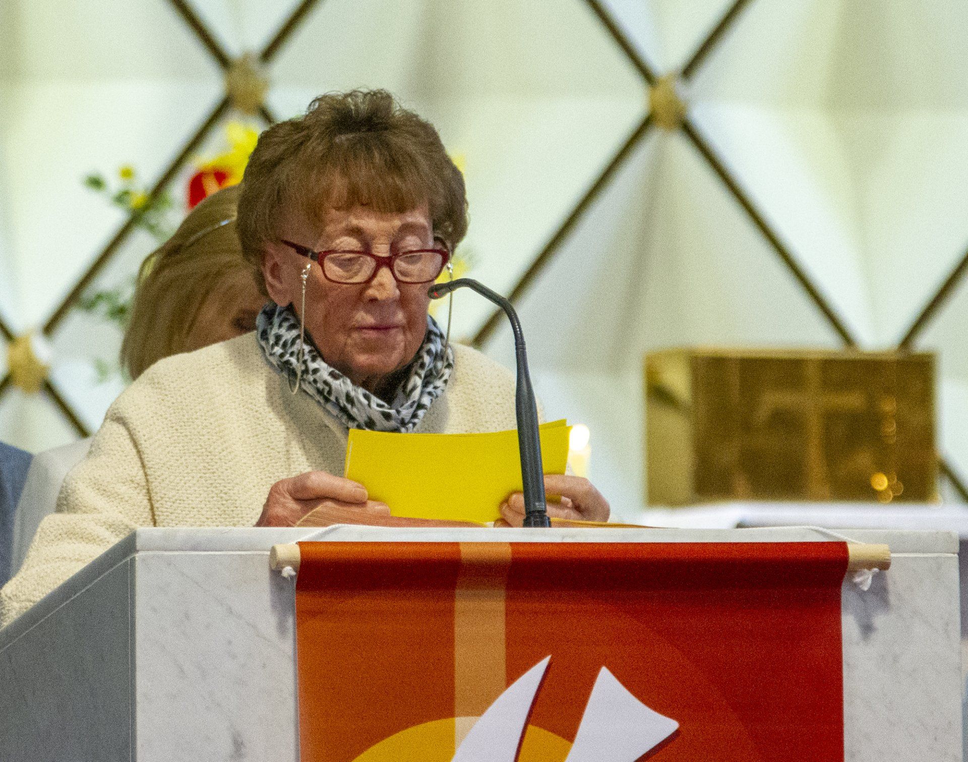 A woman is standing at a podium holding a piece of paper in front of a microphone.
