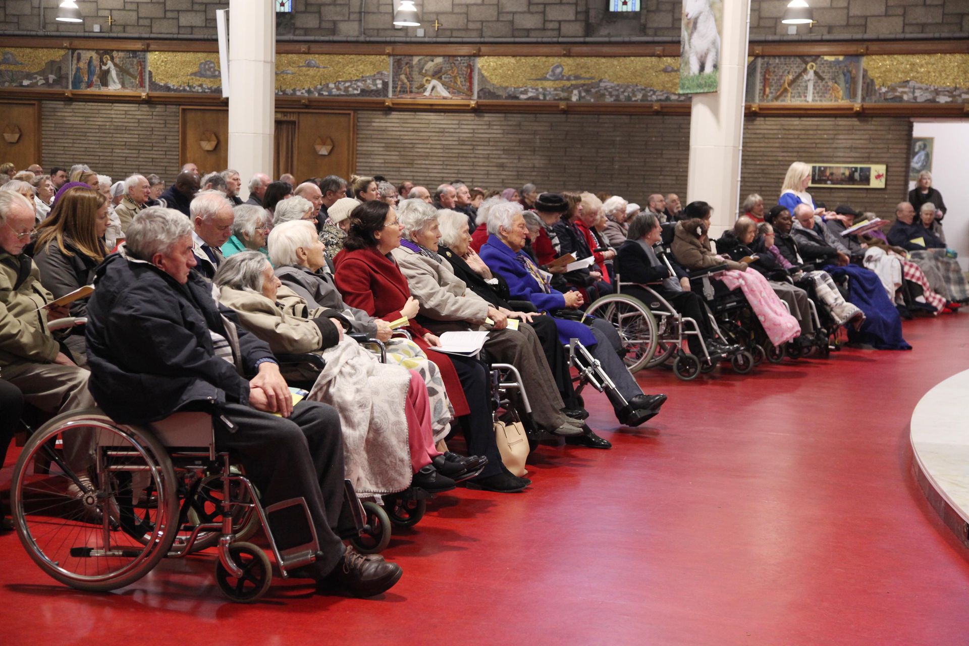 A large group of people in wheelchairs are sitting in a room.
