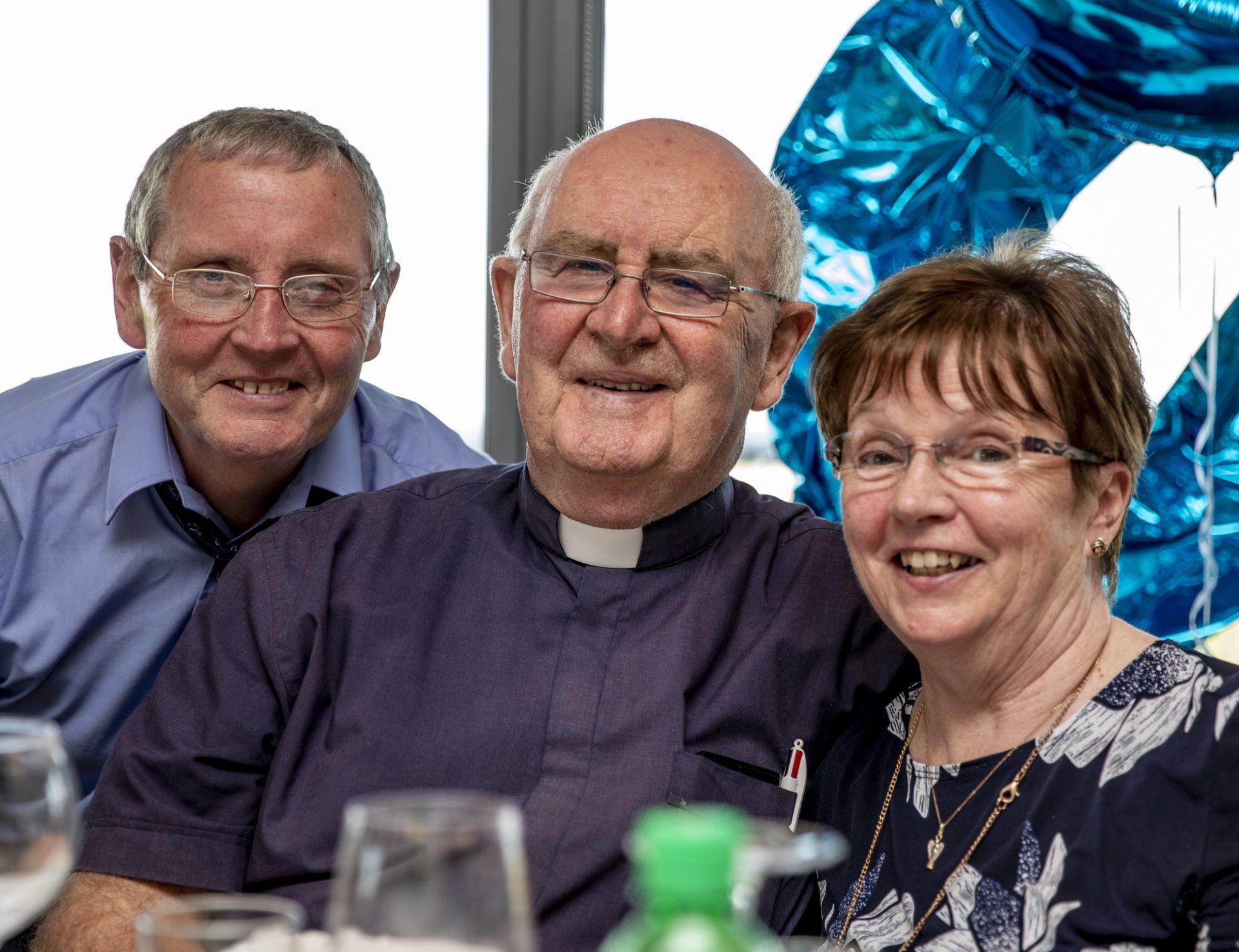 Two men and a woman are posing for a picture while sitting at a table.