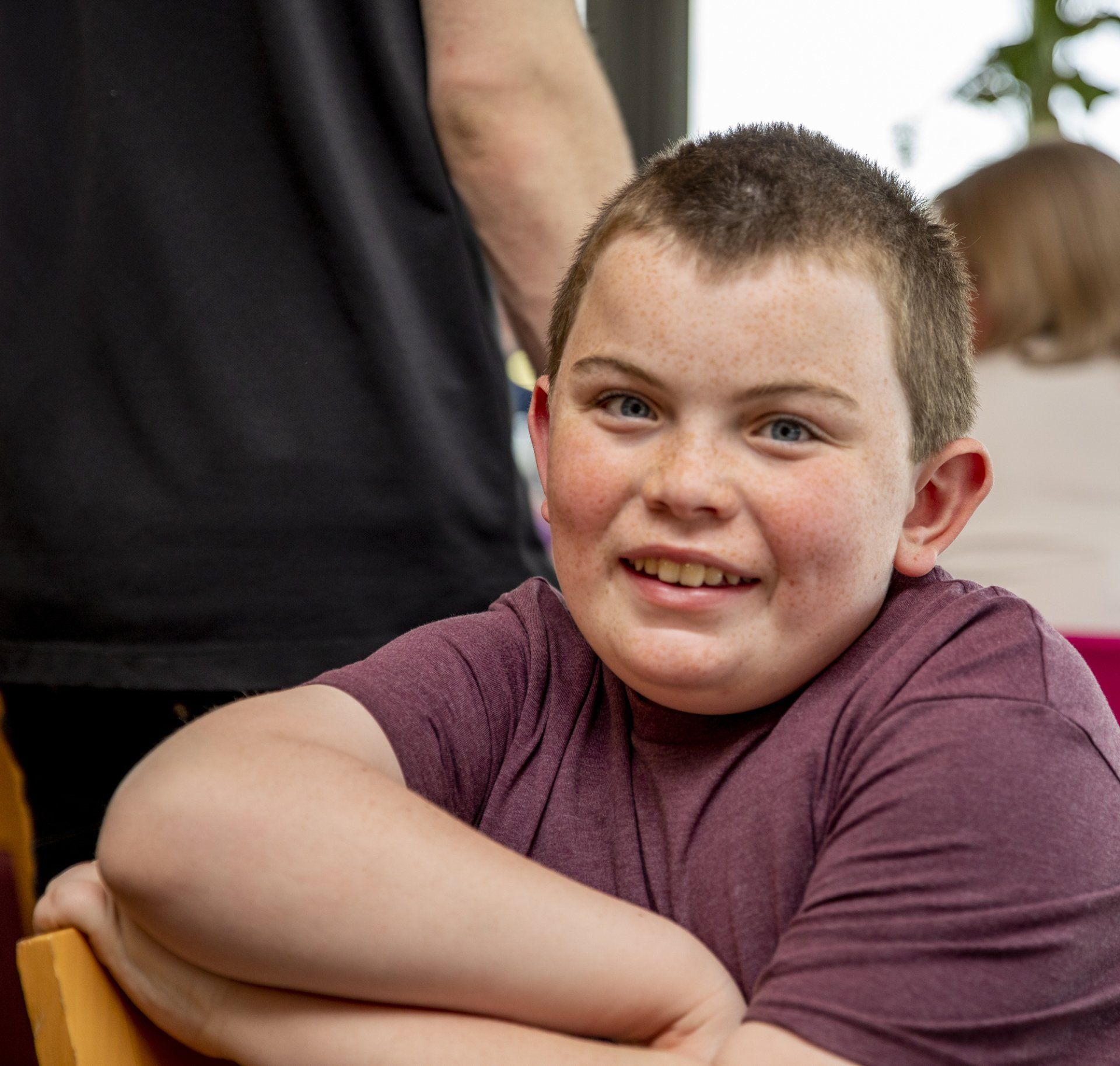 A young boy in a purple shirt is smiling for the camera