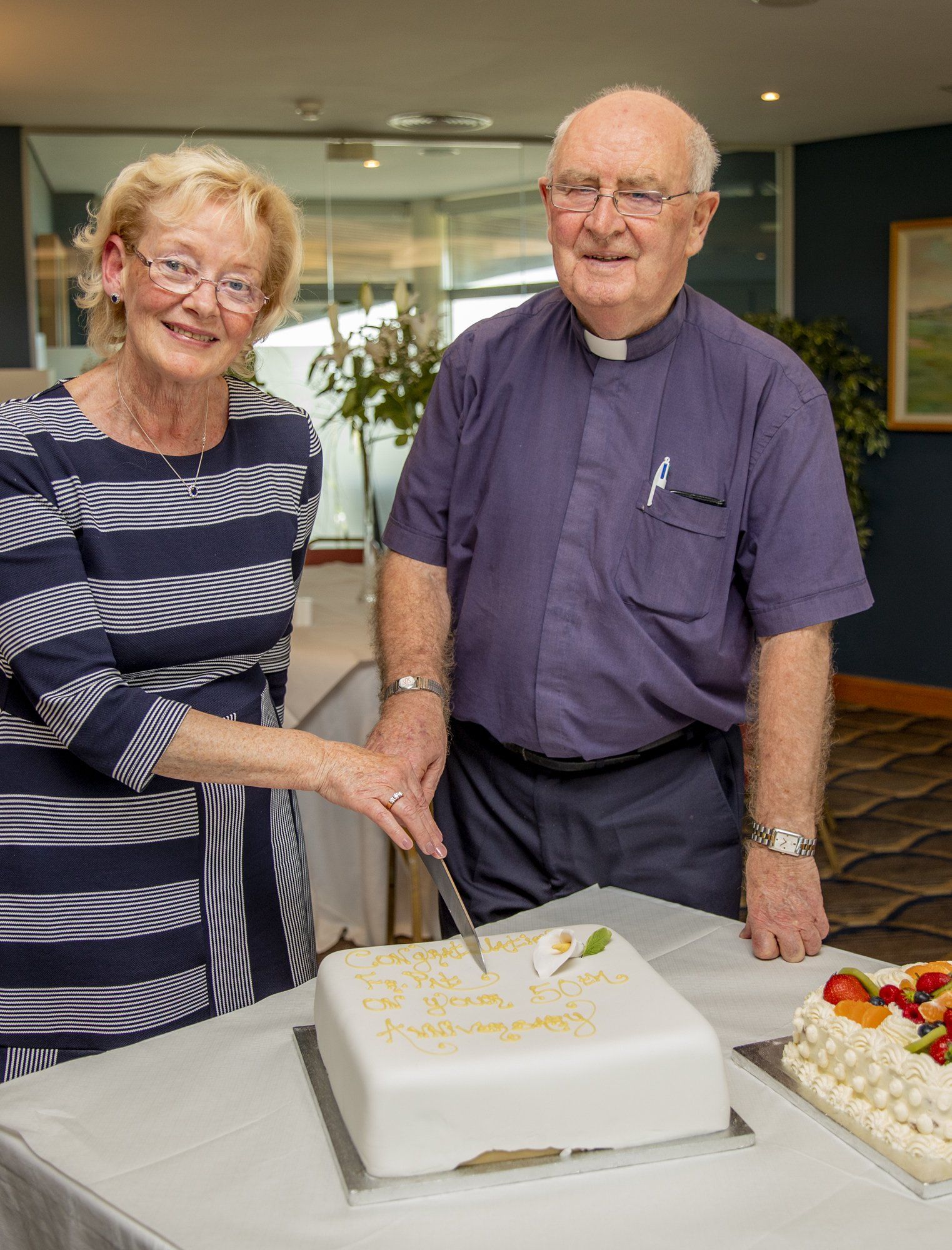 A man and a woman are cutting a cake on a table.