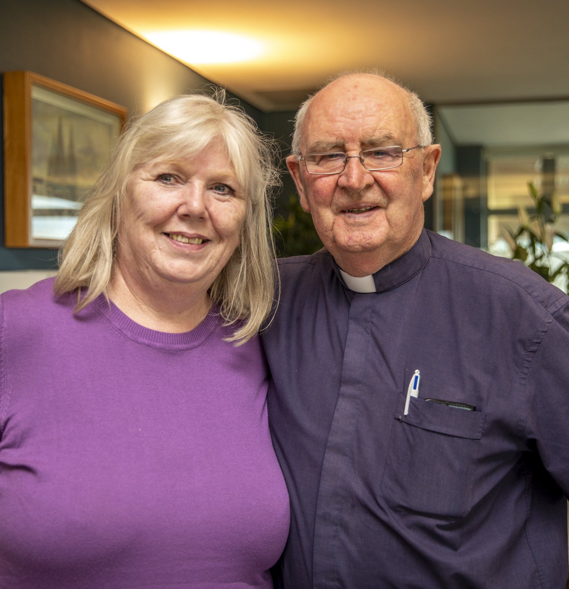 A man in a purple shirt and a woman in a purple shirt are posing for a picture.
