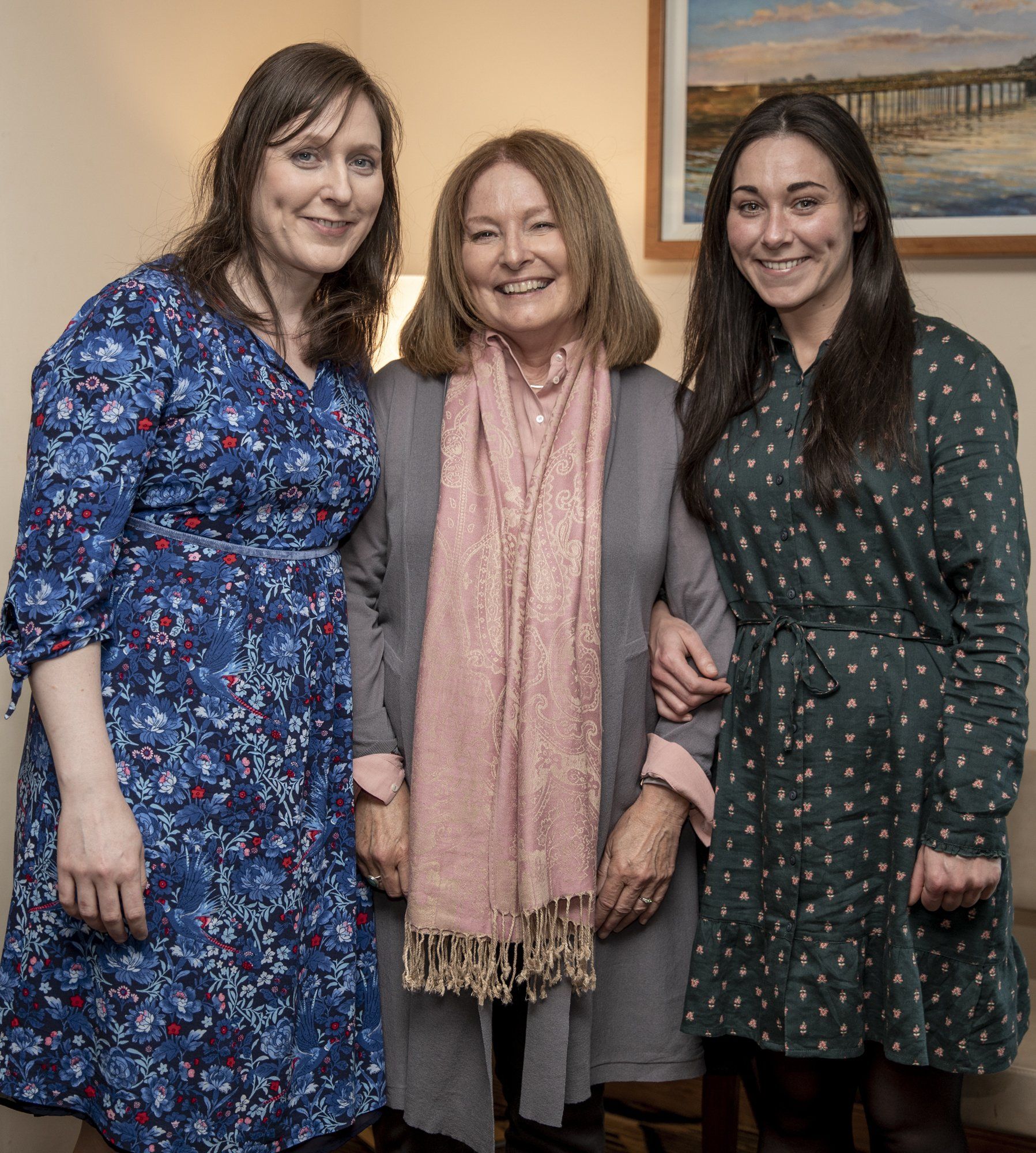 Three women are posing for a picture together in front of a painting.