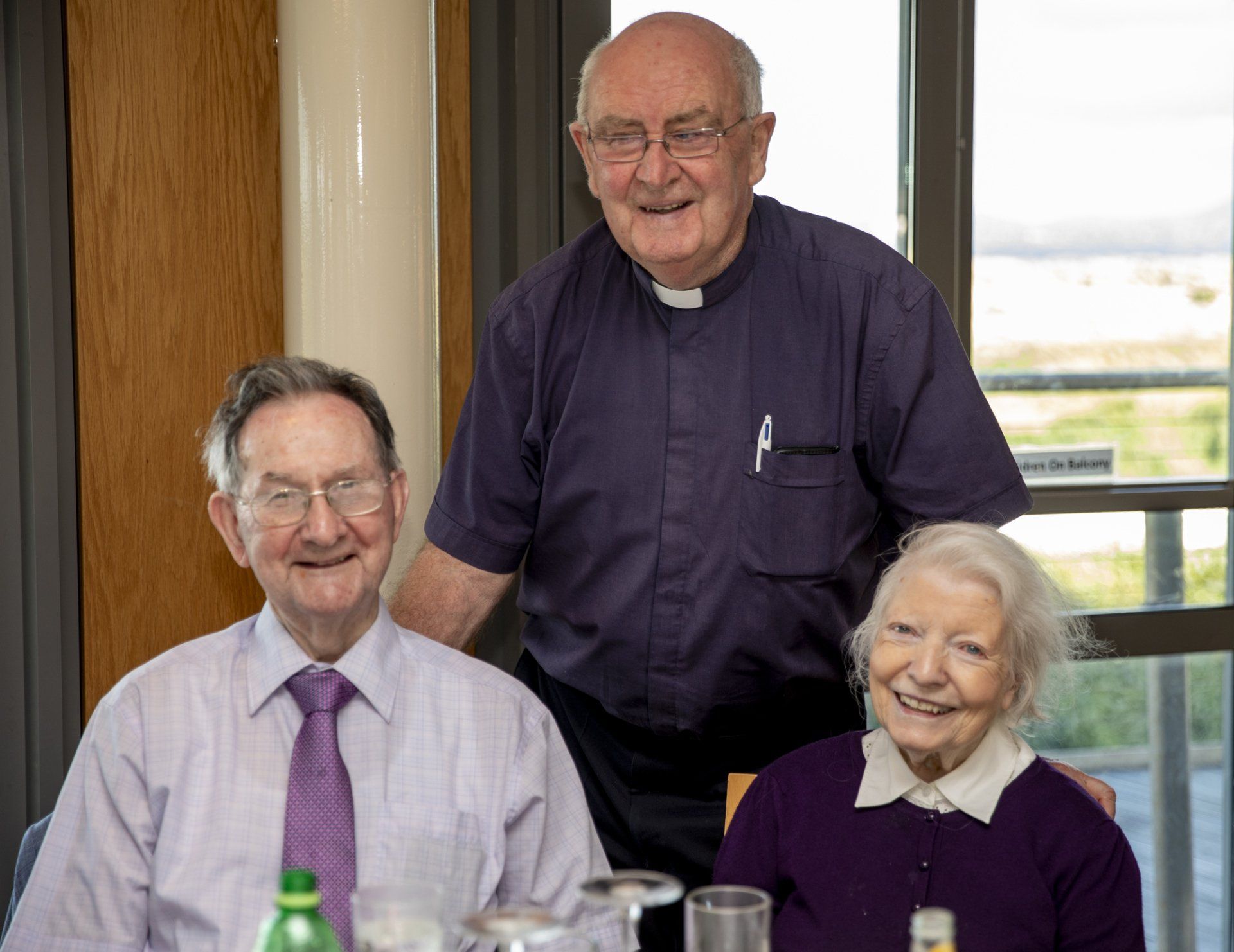Two men and a woman are posing for a picture while sitting at a table.