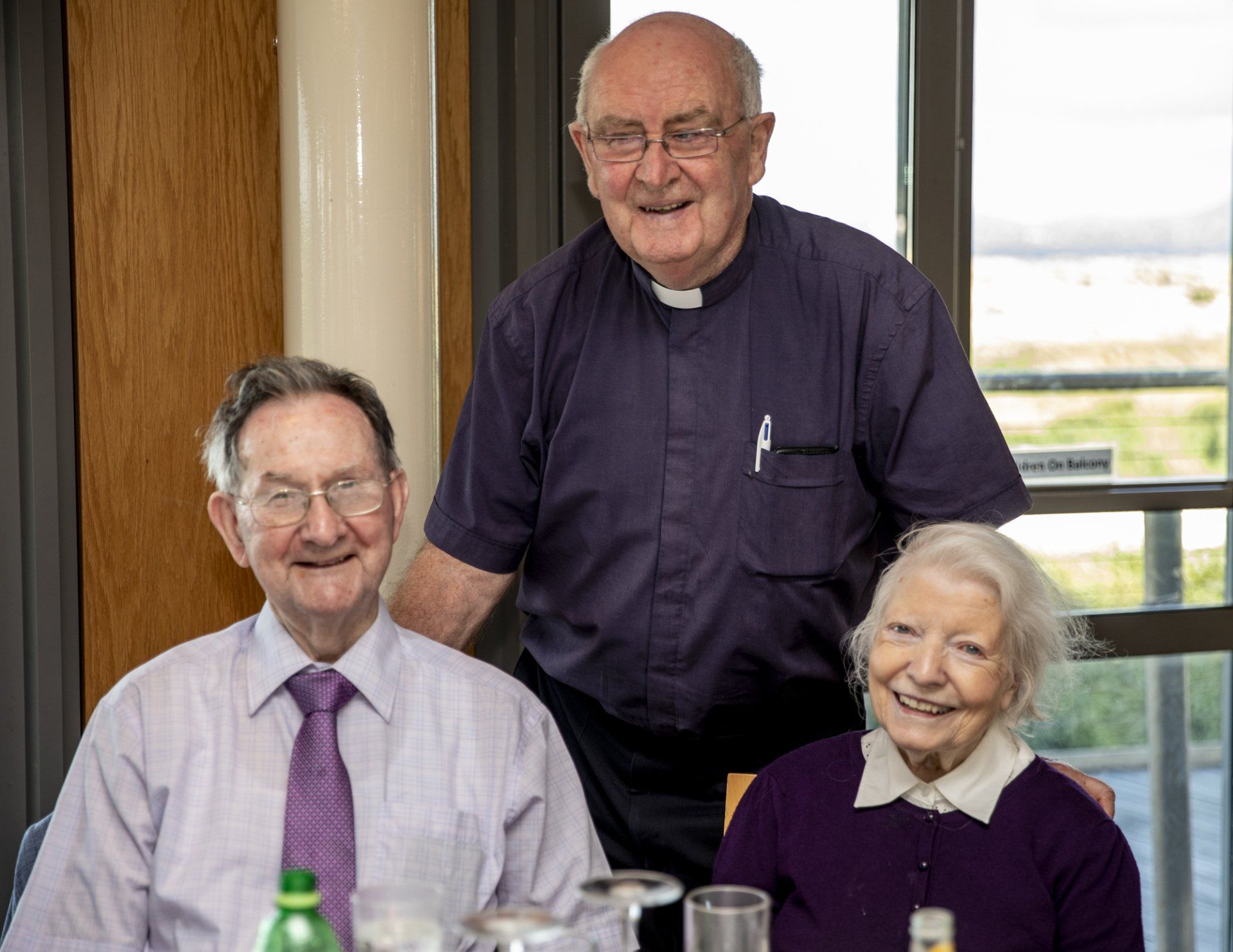 Two men and a woman are posing for a picture while sitting at a table.