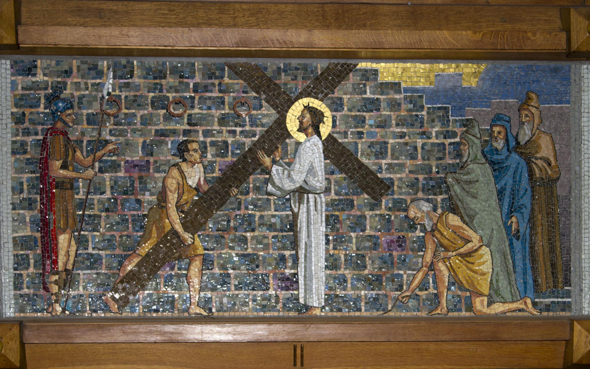 A painting of jesus carrying a cross in front of a brick wall.