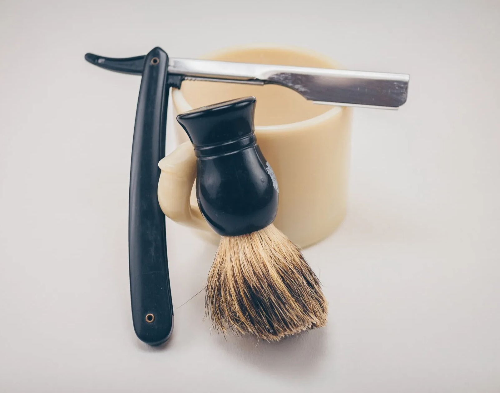 A razor and a shaving brush are sitting next to a cup of soap.