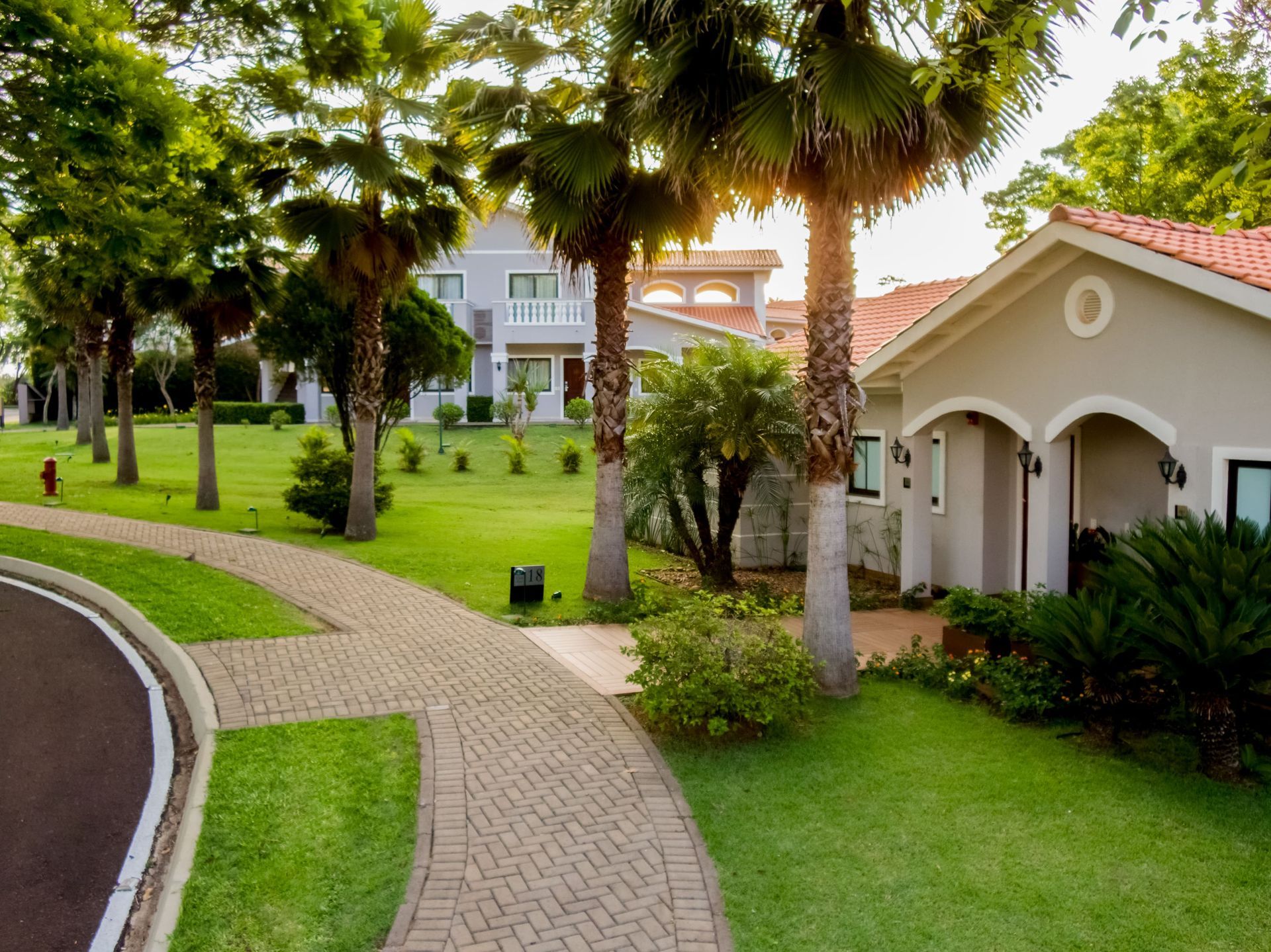 Uma passarela de tijolos leva a uma casa cercada por palmeiras