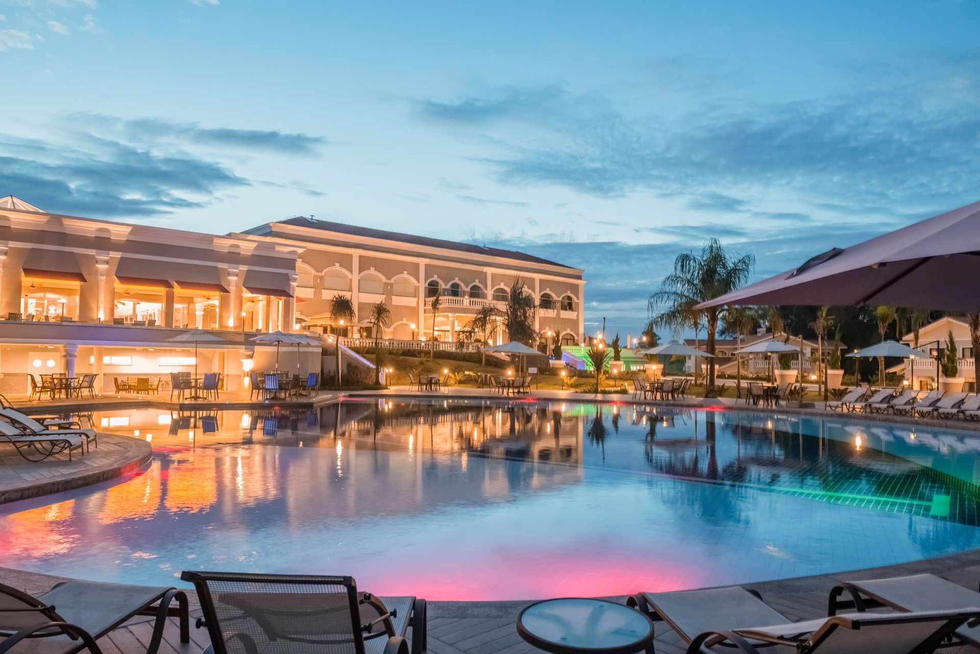 Uma grande piscina cercada por cadeiras e guarda-sóis em frente a um hotel.