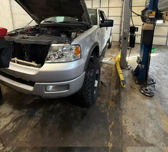 A silver Ford F-150 pickup truck with its hood open in an auto repair shop next to a car lift. | Russell's Garage
