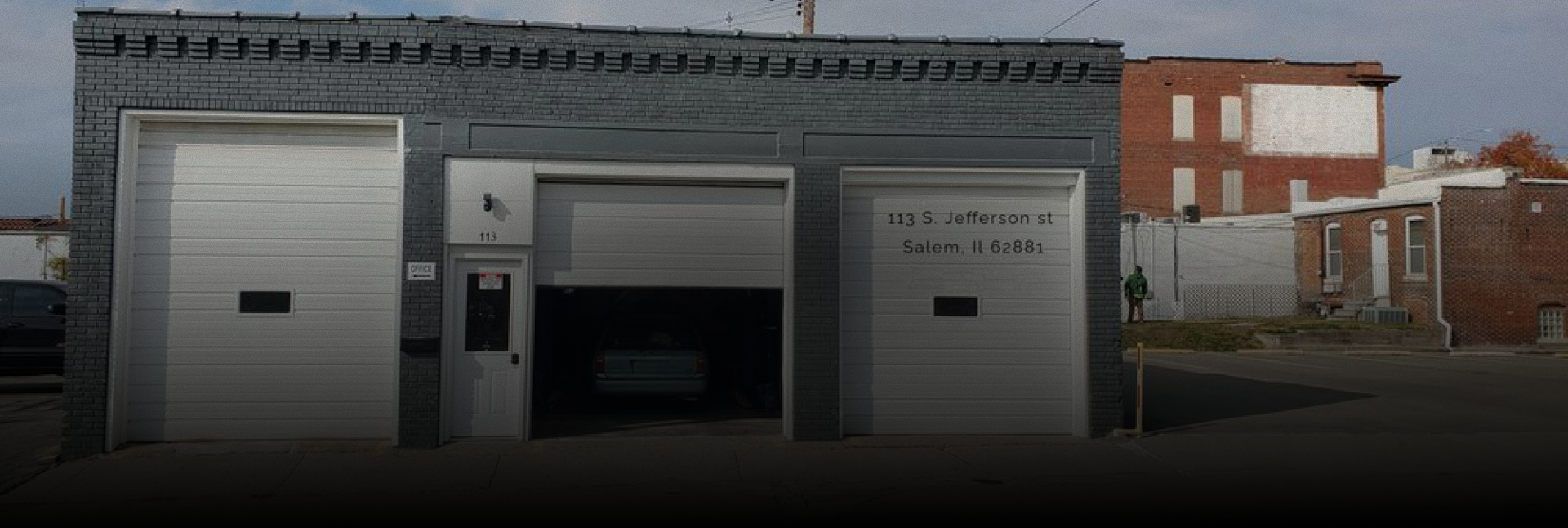 A grey industrial building with three white garage doors and a central entrance door, under a clear sky. | Russell's Garage