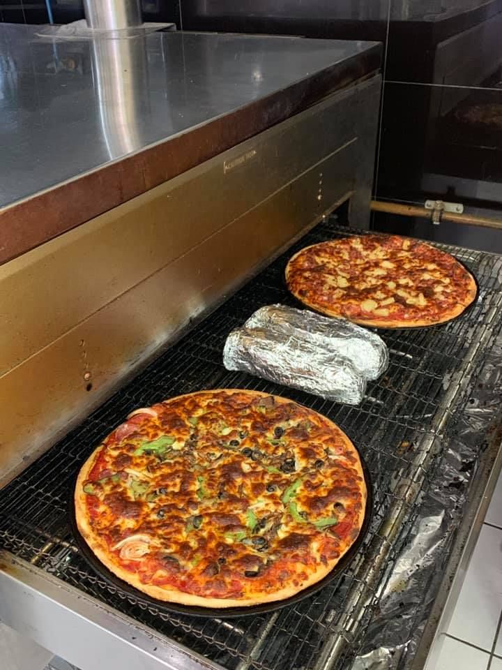 Three Pizzas Are Sitting On A Conveyor Belt In A Kitchen — Michelangelo's Pizza & Pasta in Kirwan, QLD
