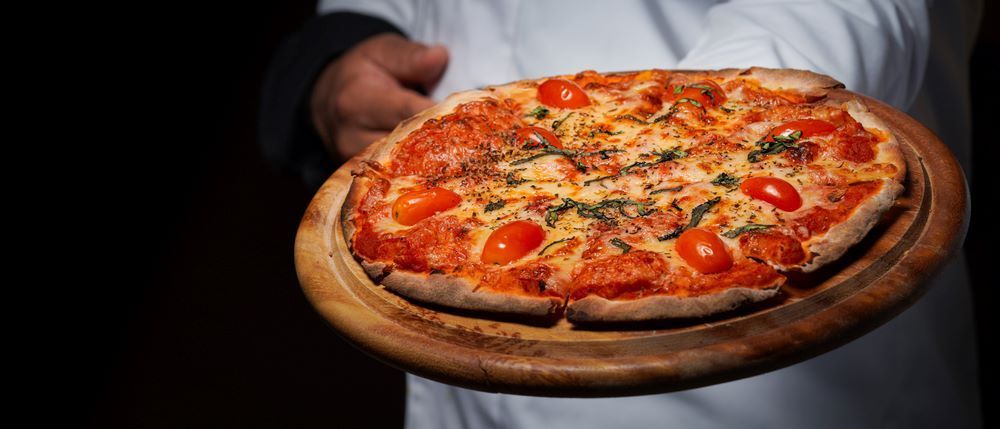 A Man is Holding a Pizza on a Wooden Cutting Board — Michelangelos Pizza & Pasta in  Hermit Park, QLD