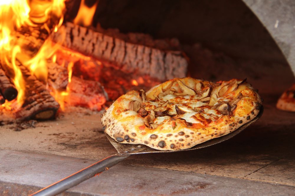A Pizza is Being Taken Out of an Oven With a Spatula — Michelangelos Pizza & Pasta in  South Townsville, QLD