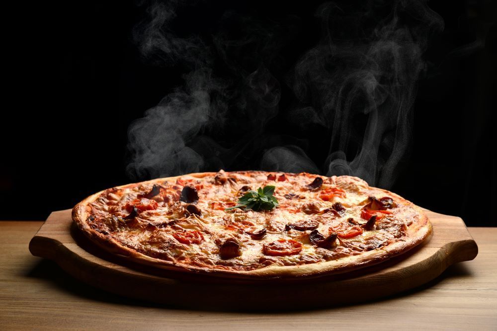 A Pizza is Sitting on a Wooden Cutting Board With Steam Coming Out of It — Michelangelos Pizza & Pasta in  Burdell, QLD