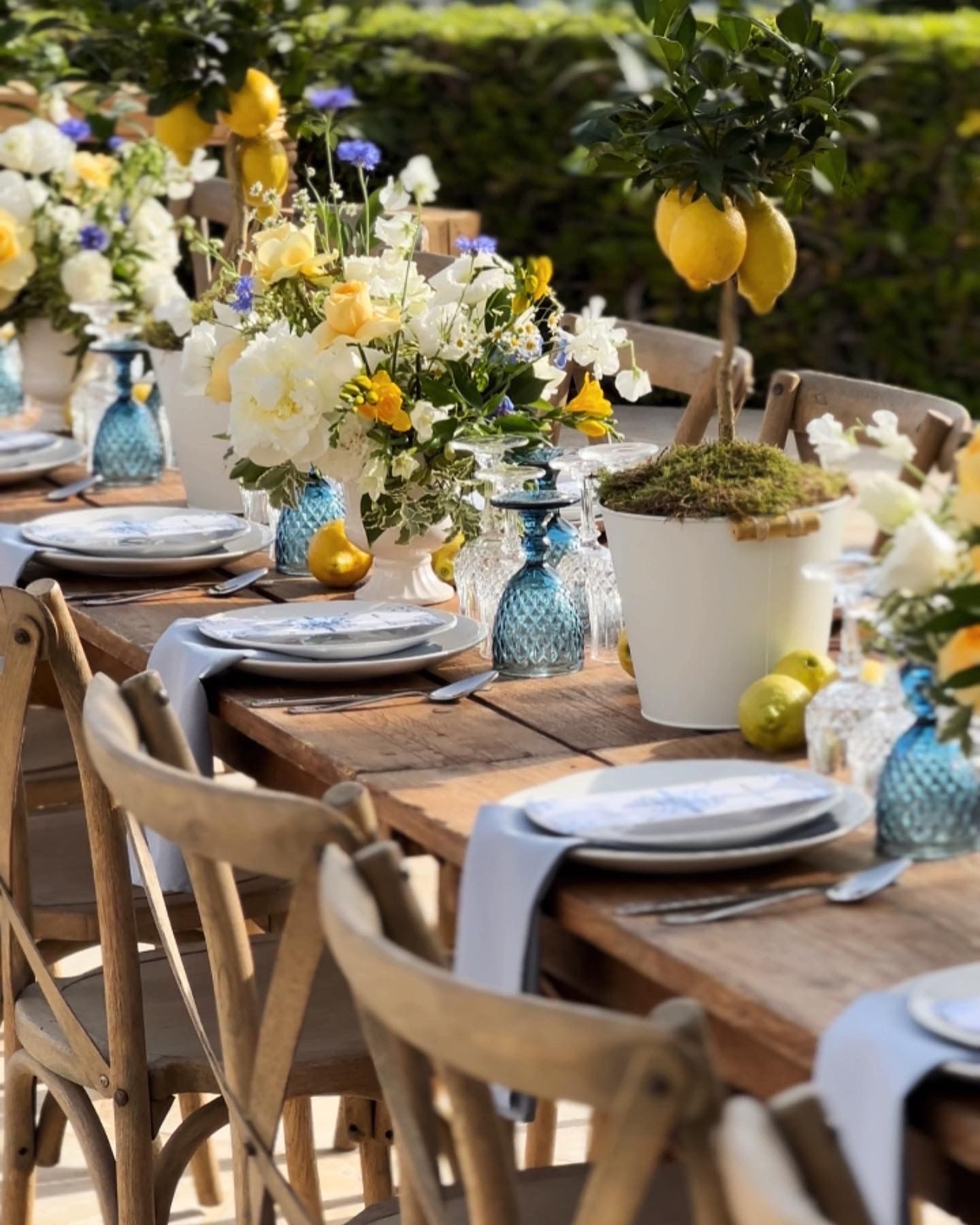 A long wooden table with plates , utensils , and flowers on it.