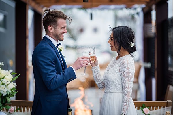 a bride and groom are toasting with champagne in front of a fire .