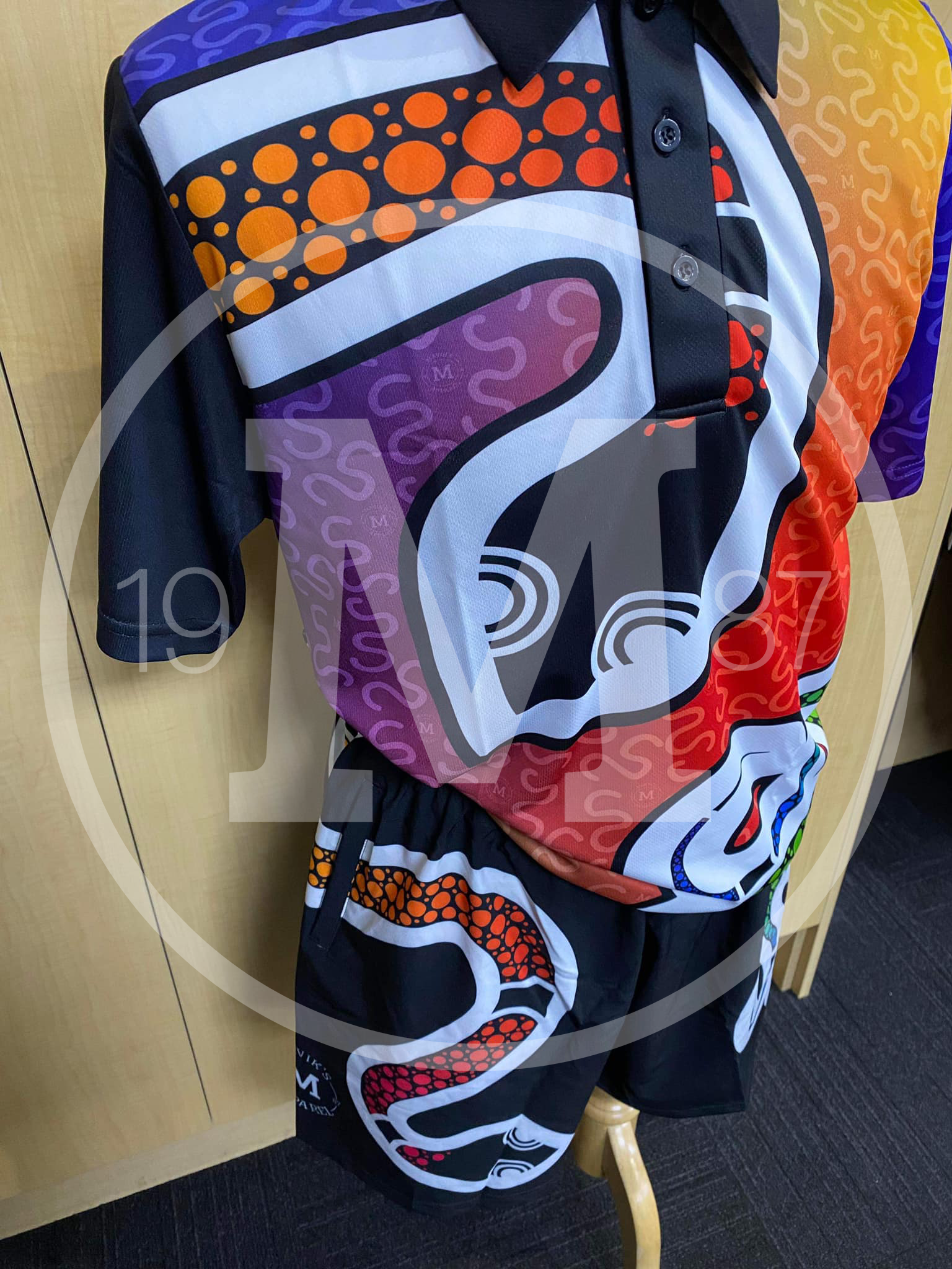 A mannequin wears a polo shirt and matching shorts featuring vibrant, colorful Indigenous Australian dot art designs.