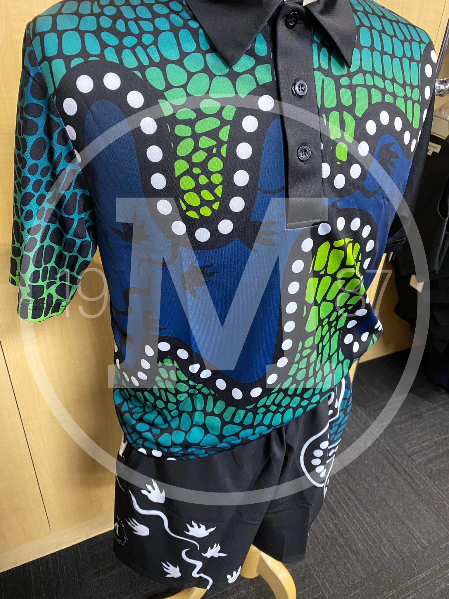 A polo shirt and matching shorts with a blue and green scale-like pattern and white dotted lines, displayed on a mannequin.