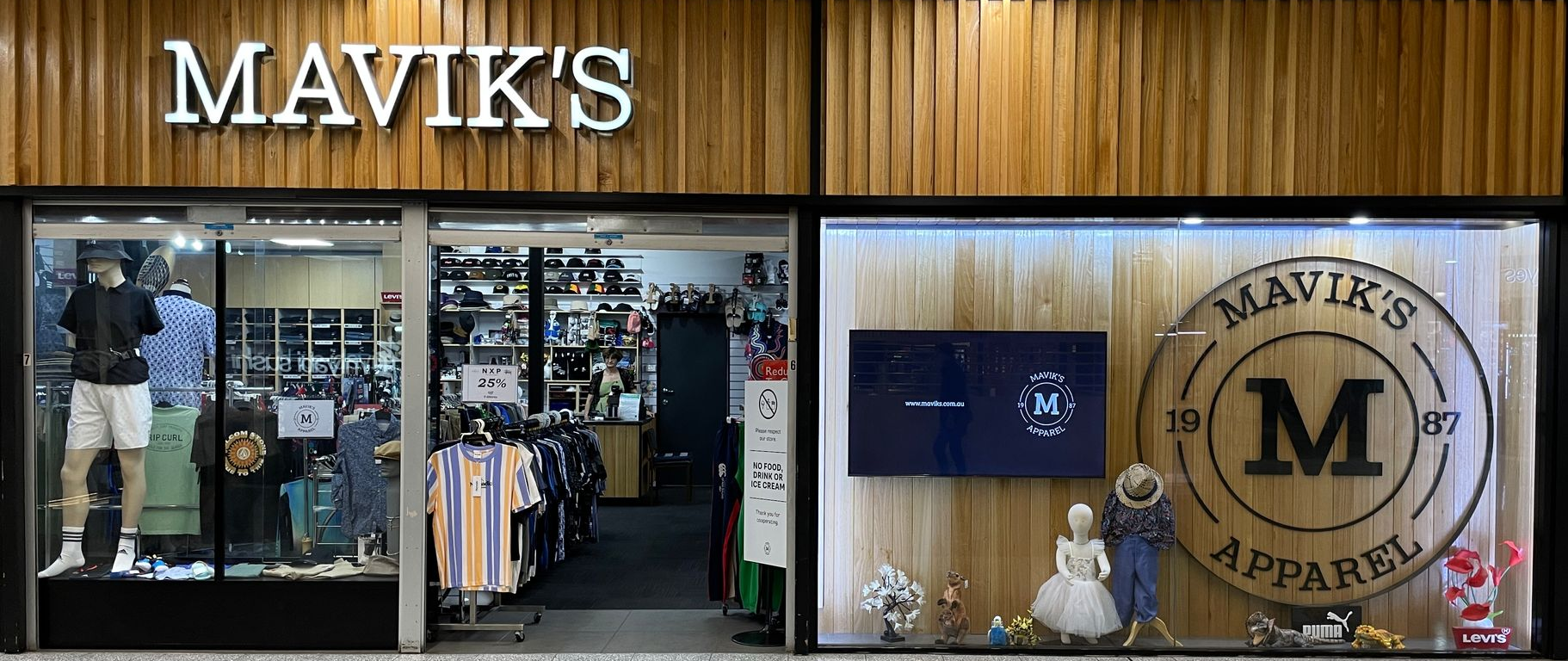 Two people stand smiling in front of a large, circular wooden sign for