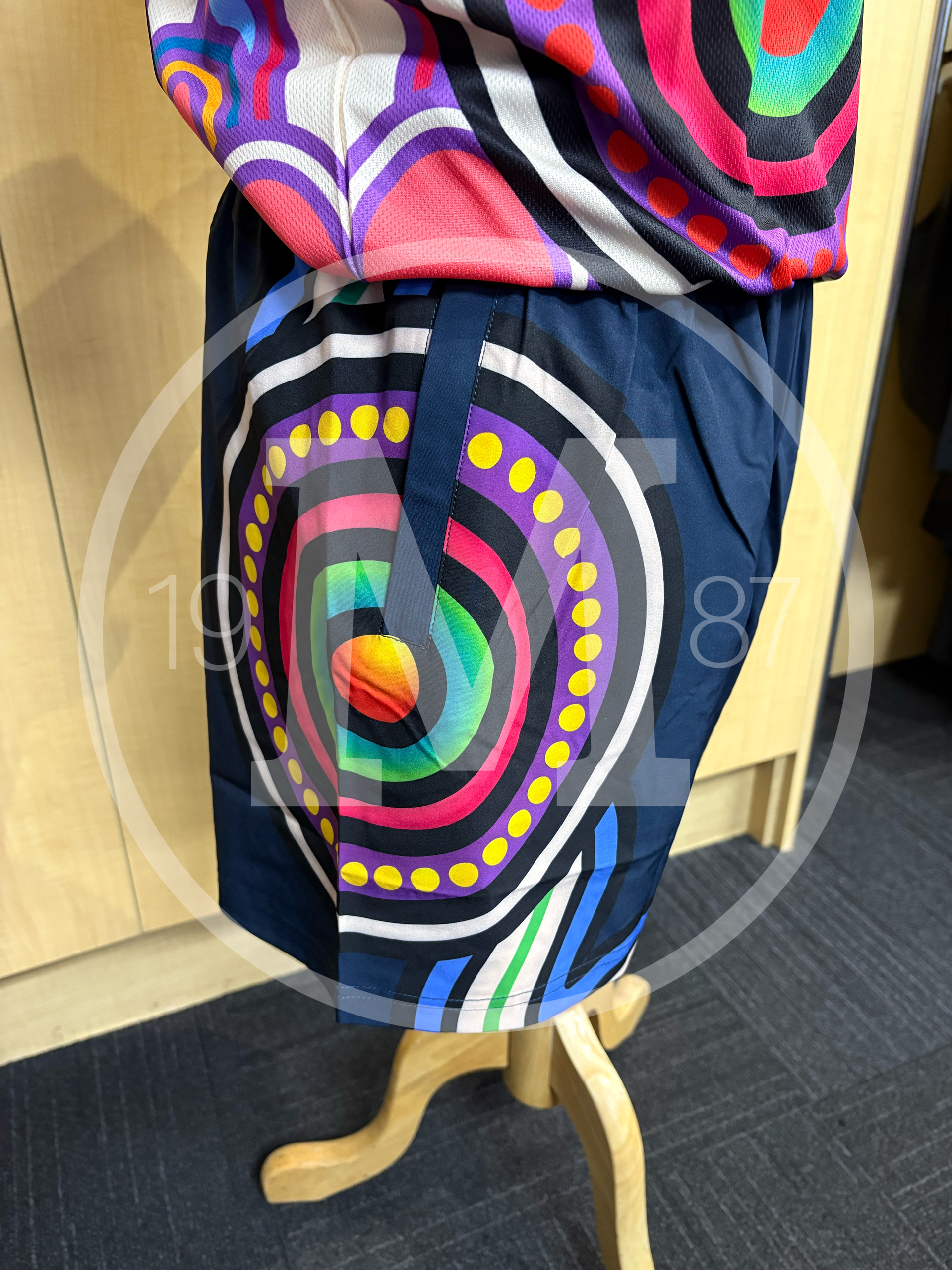 A mannequin torso wearing shorts with a vibrant, multi-colored circular bullseye design on a dark blue background.