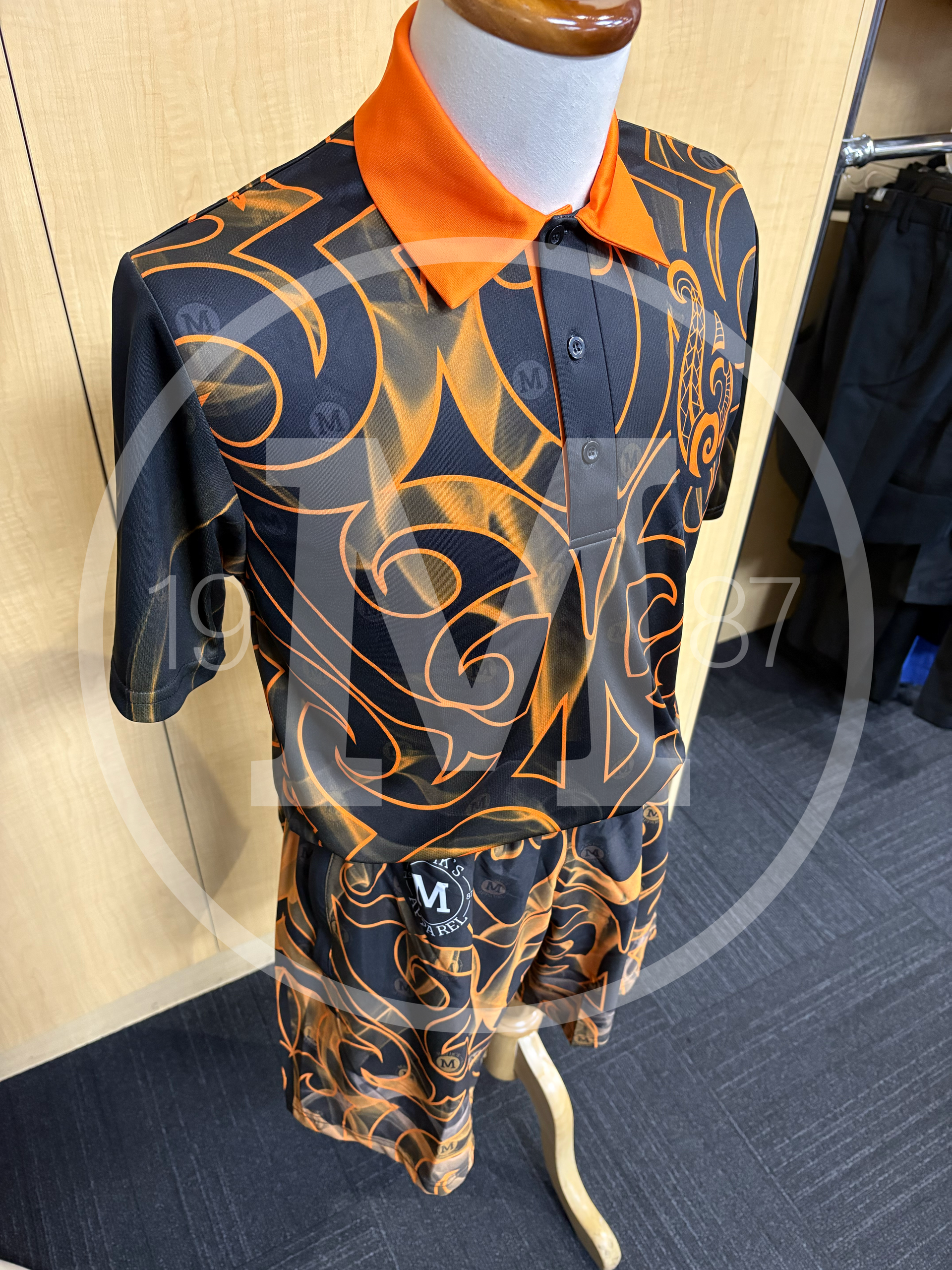 A black and orange patterned polo shirt and matching shorts set displayed on a mannequin inside a retail store.