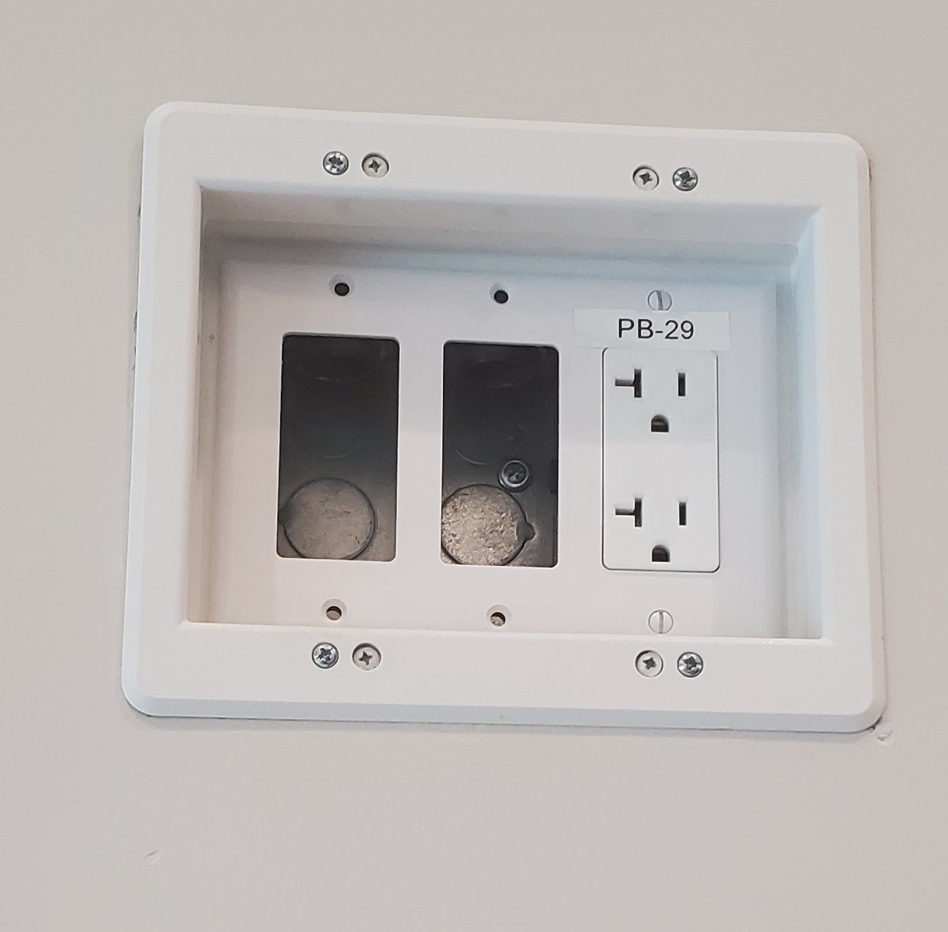 White recessed wall plate with two empty holes and one electrical outlet.