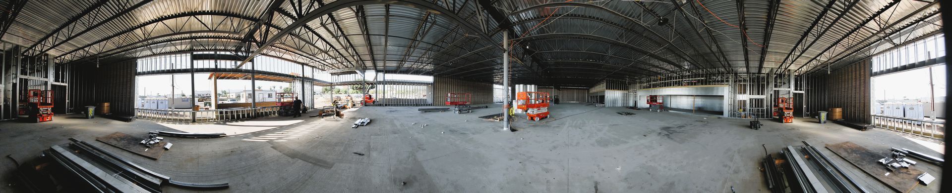 Interior of a large building under construction. Concrete floor, steel beams, large windows, and construction materials.
