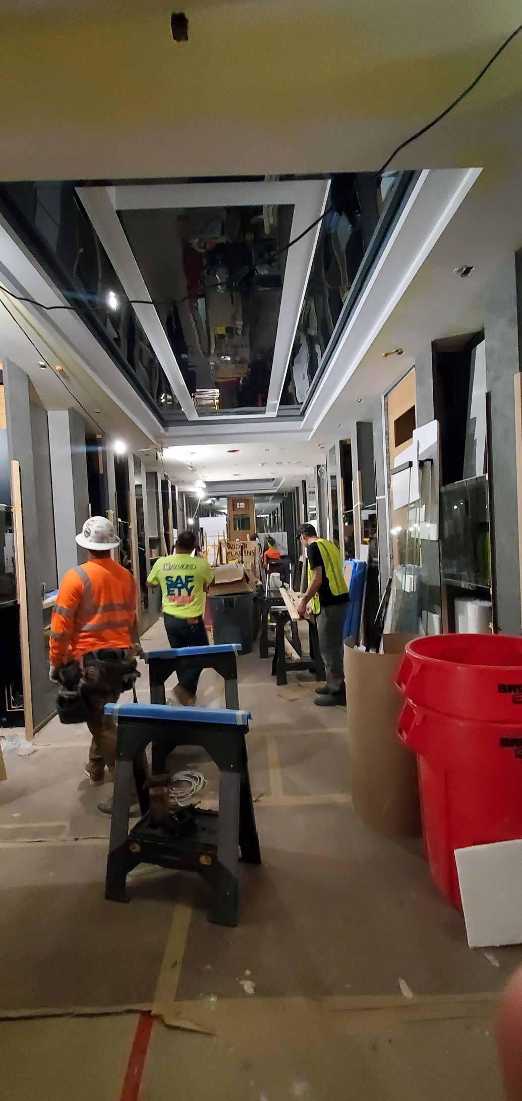 Construction workers inside a hallway with a mirrored ceiling. Some workers are wearing safety vests.