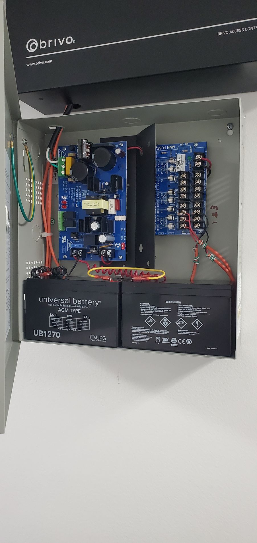 Open security system panel with circuit boards, wires, and two batteries.