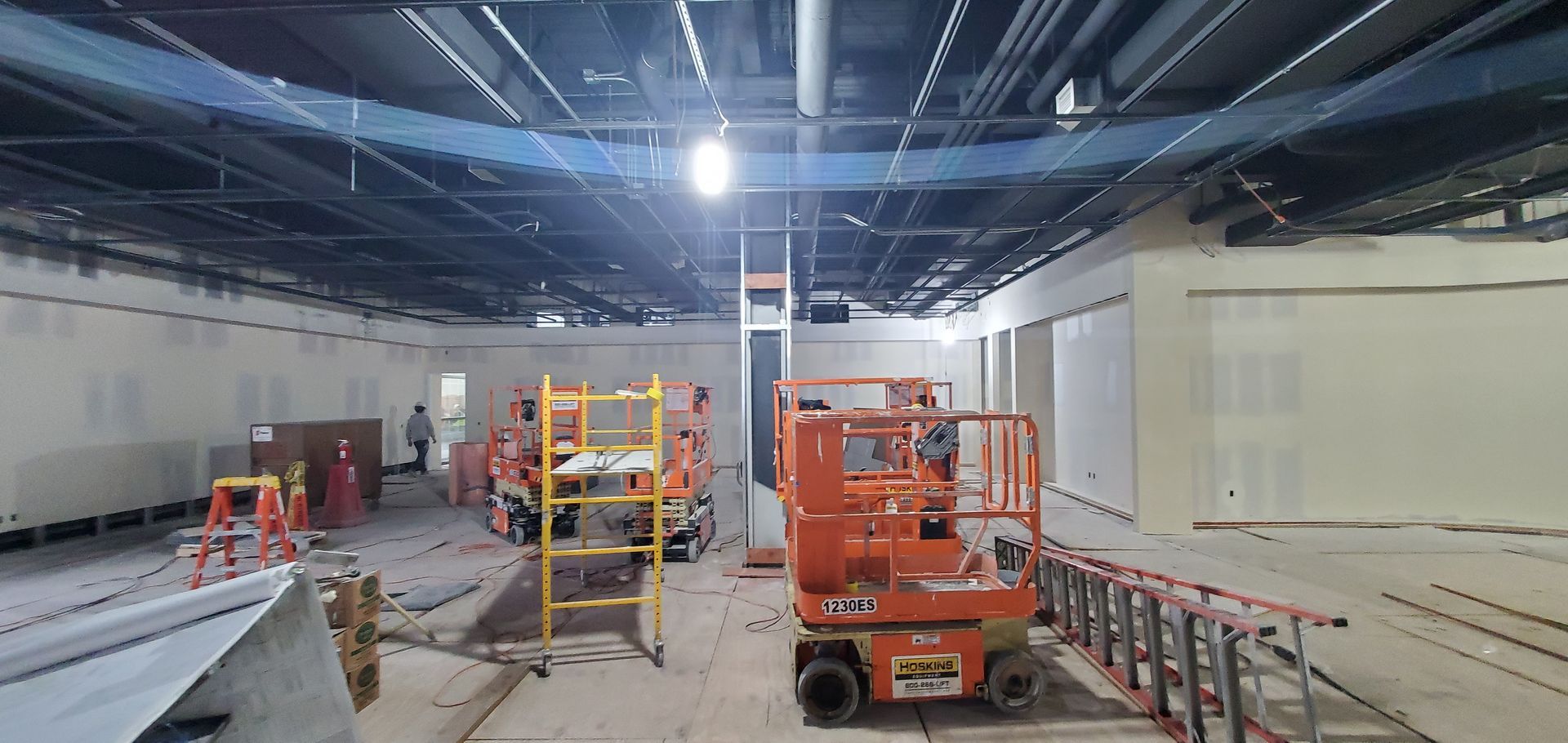 Interior construction site with workers, equipment, unfinished walls, and ceiling structures.