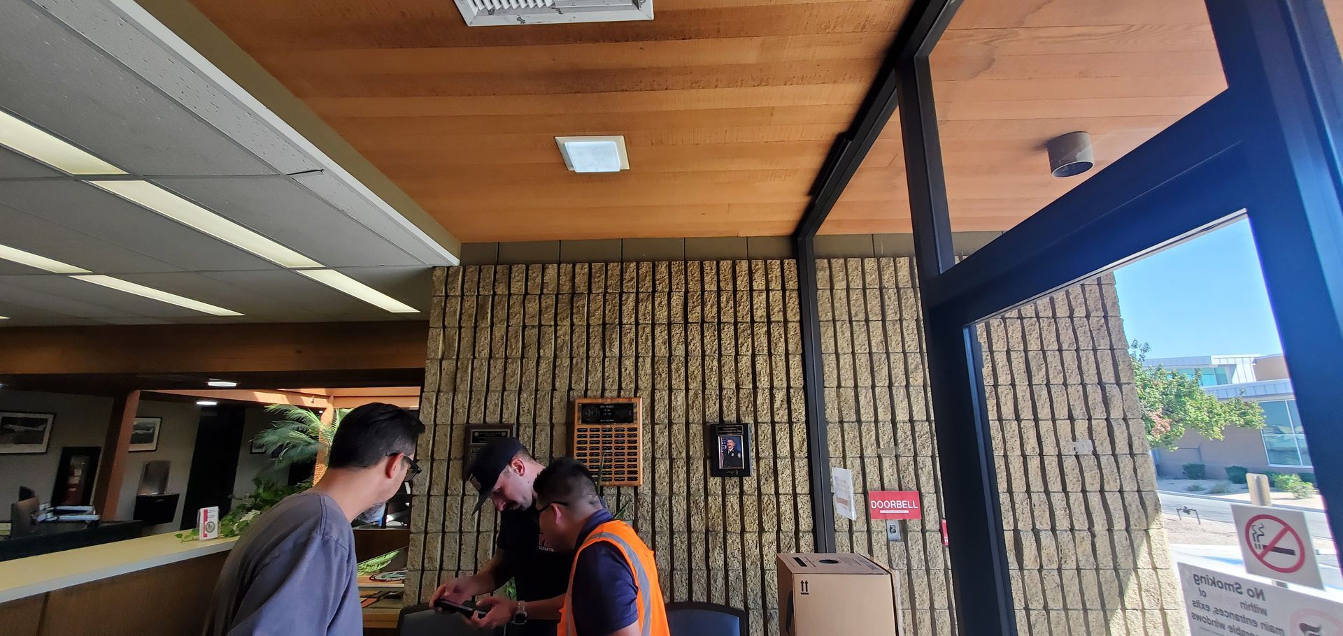 Three people stand inside a building, looking down at something. A door is open to the right.