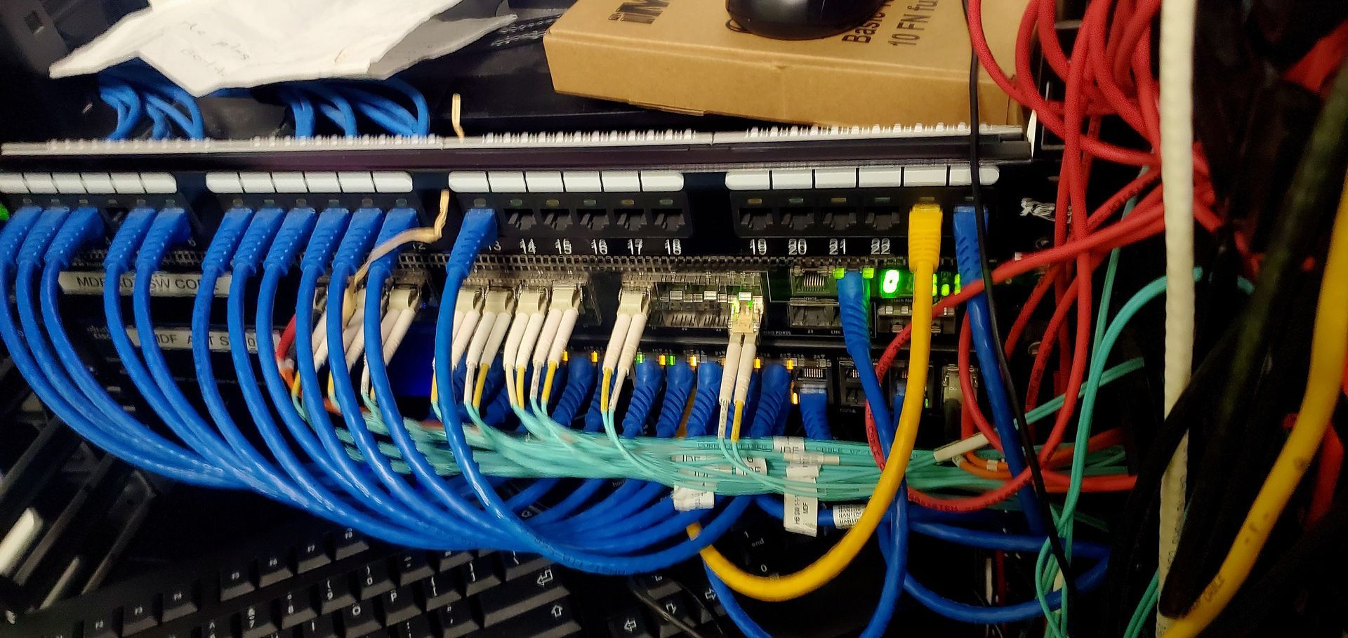 Network cables connected to a patch panel and switch, blue, yellow, and red cables.