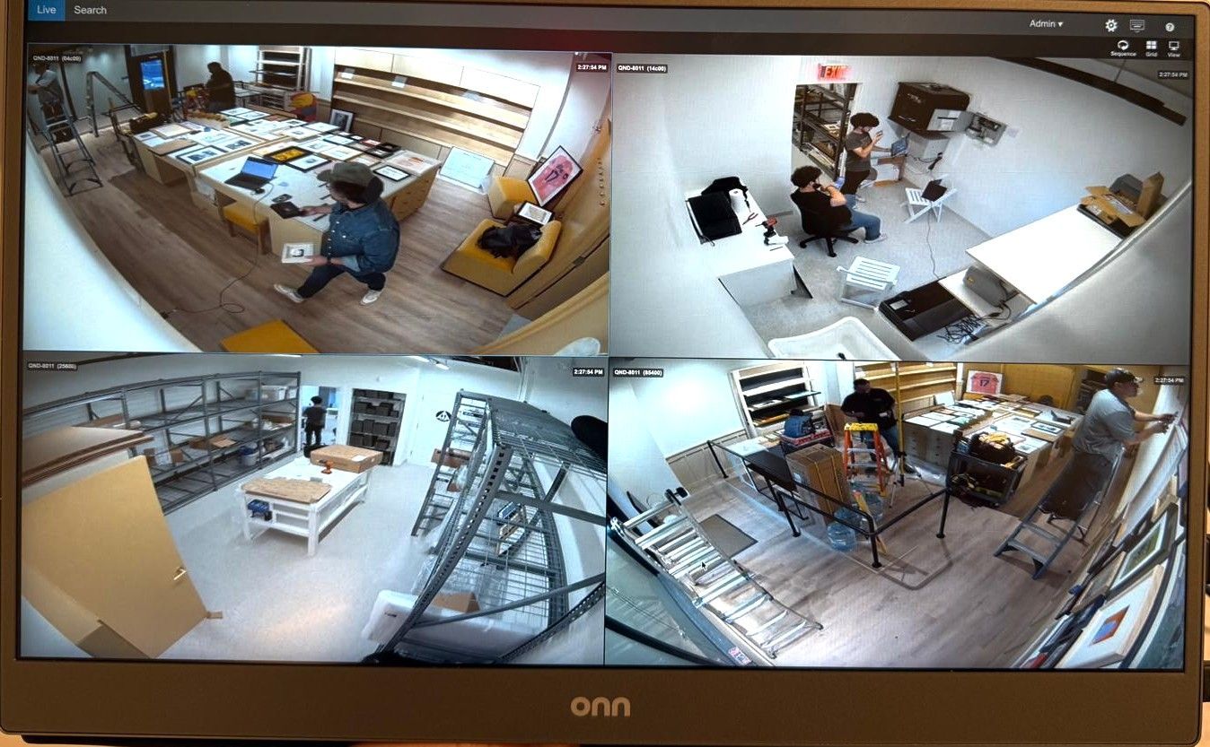 Four-way split screen showing security camera views of an interior: people, furniture, shelves, and artwork.