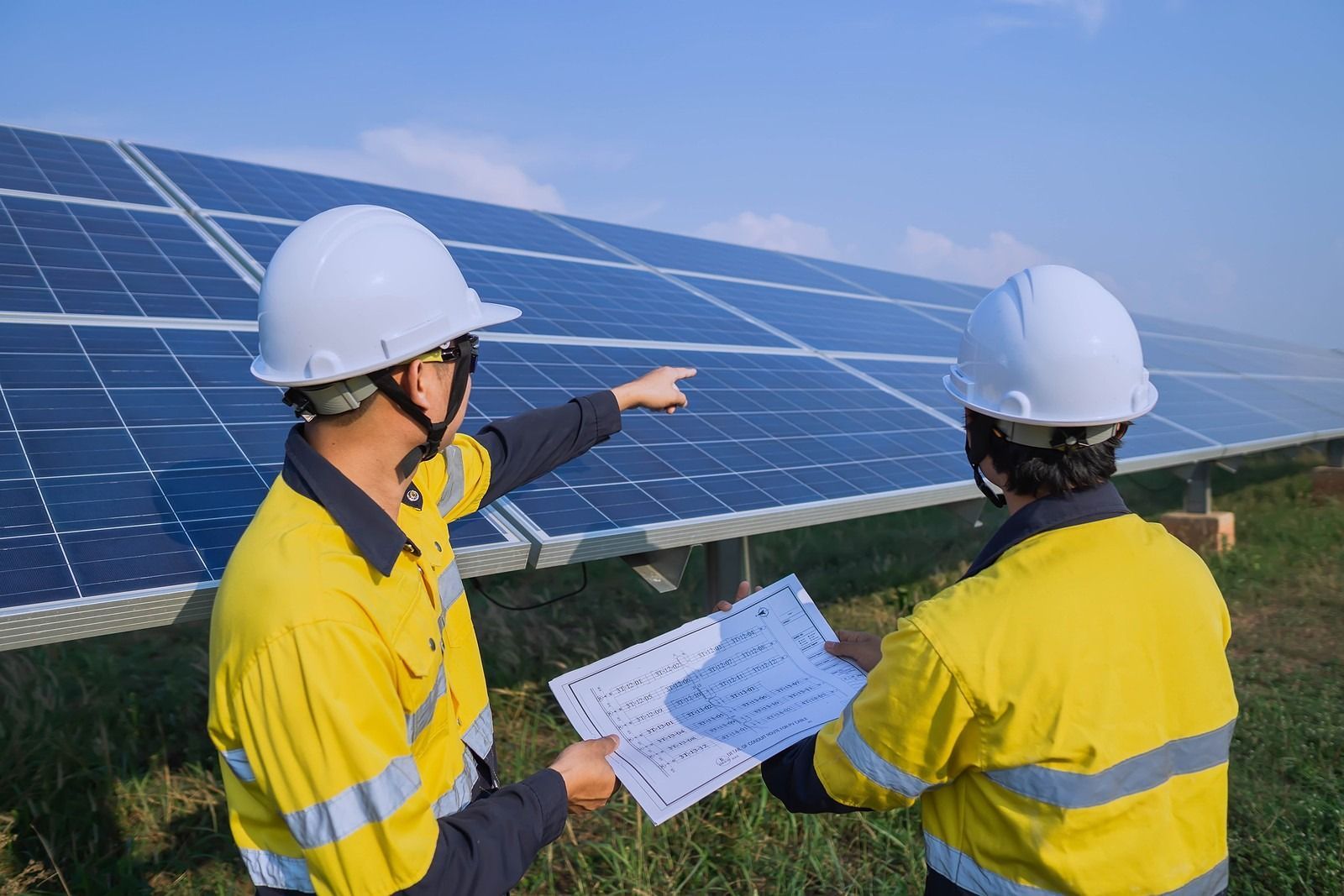 Two workers in yellow vests and hard hats examining solar panels.