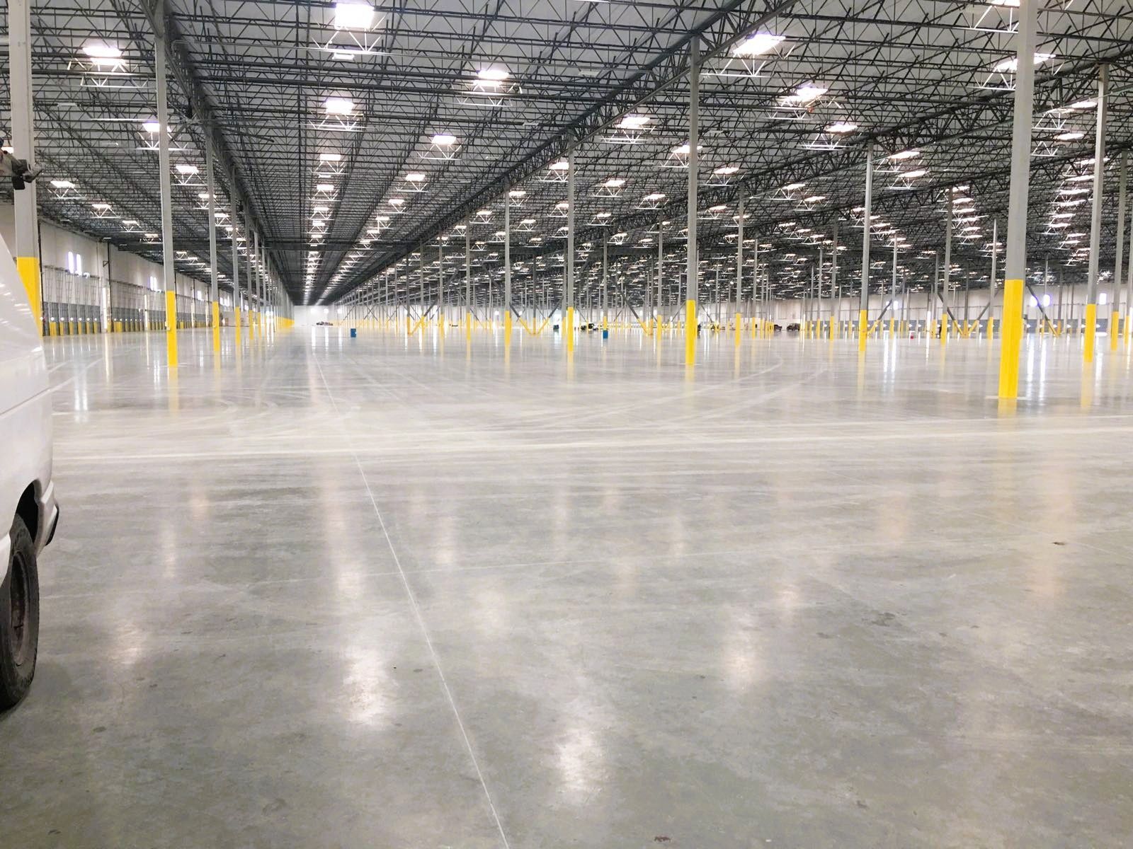 Wide, empty warehouse with concrete floor, high ceiling, and metal beams. Yellow safety poles line the interior.